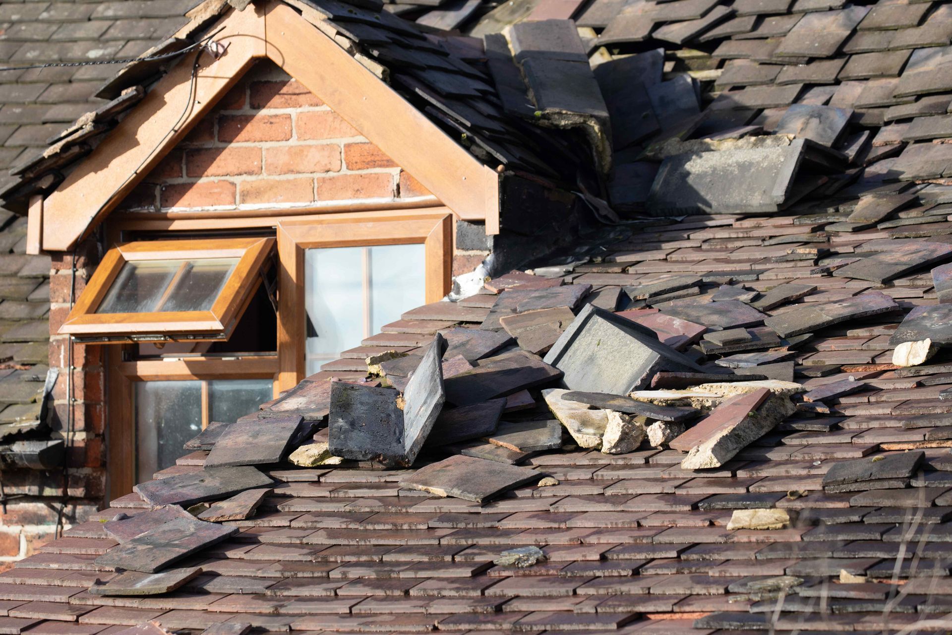 A deteriorating roof sits in disrepair cluttered with broken shingles and all other forms of debris.
