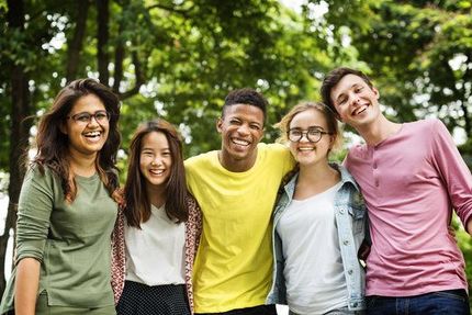 Group of students and a woman posing in a classroom; smiling, wearing jeans, and various shirts.