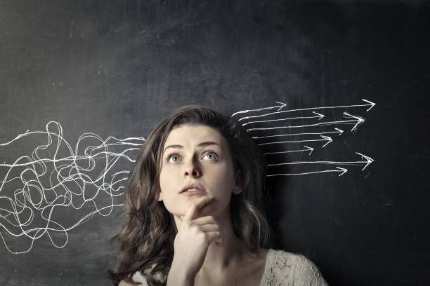 Woman in glasses, blue sweater, holding laptop, looking at the camera against a blue background.