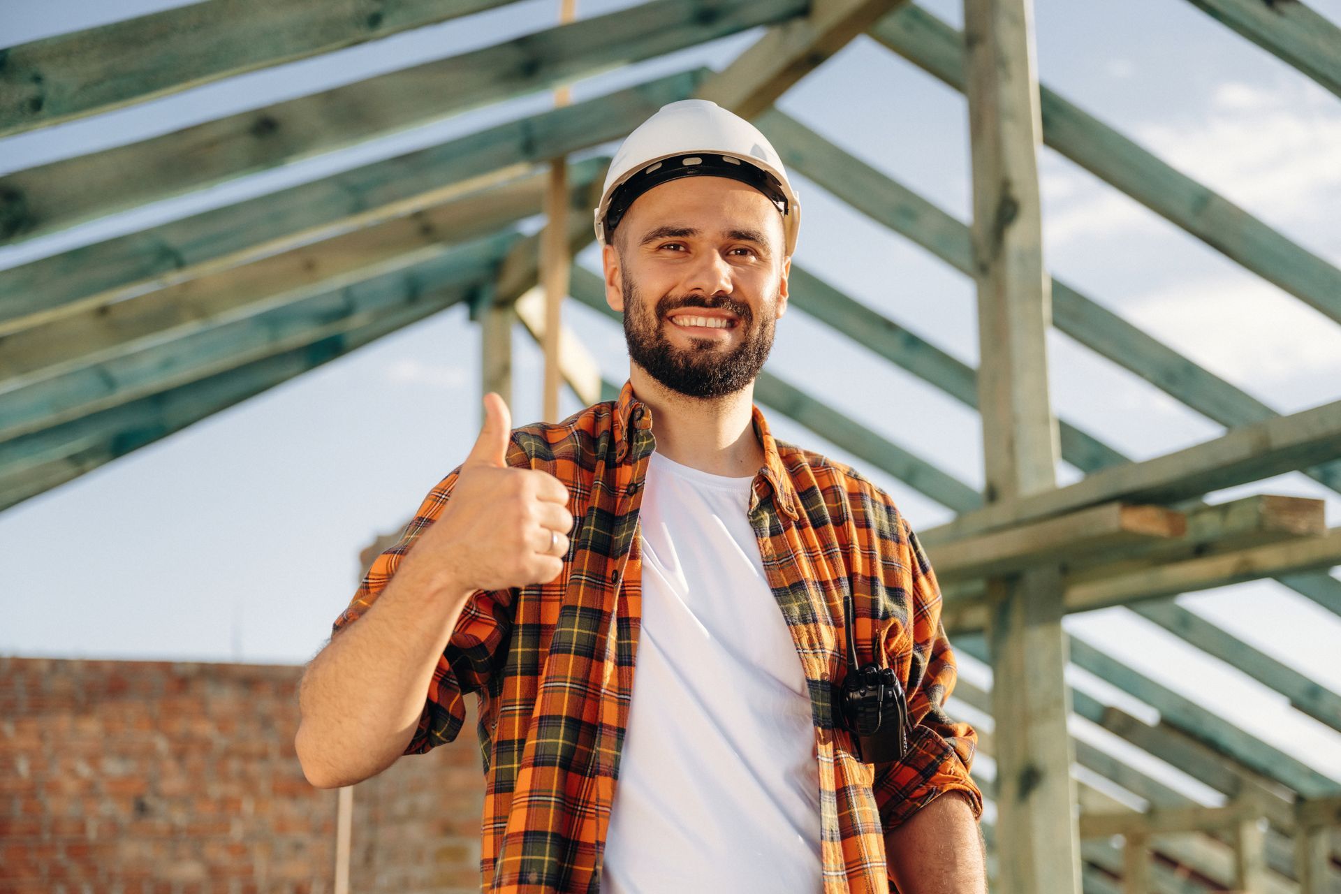 A construction worker showing a thumbs-up and smiling in a roof installation site.