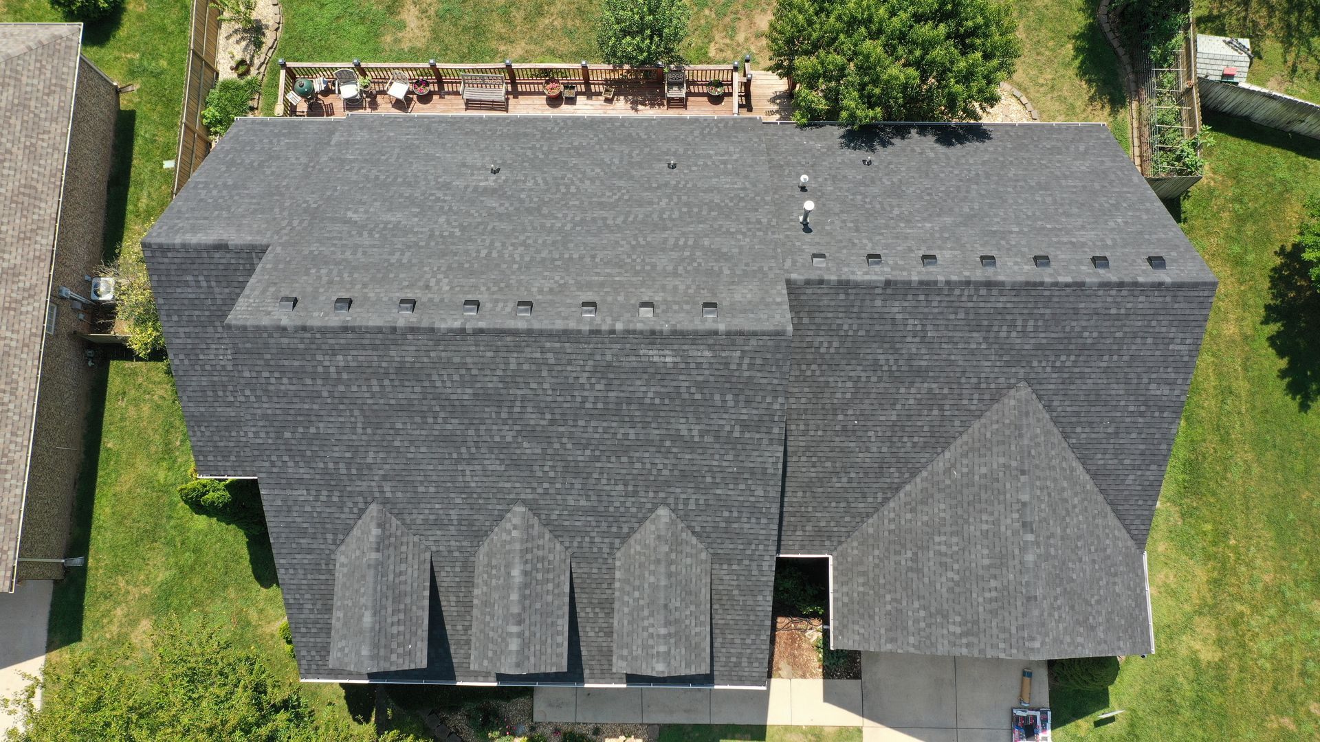 Overhead view of a house with a dark gray shingled roof, dormers, and a green lawn.