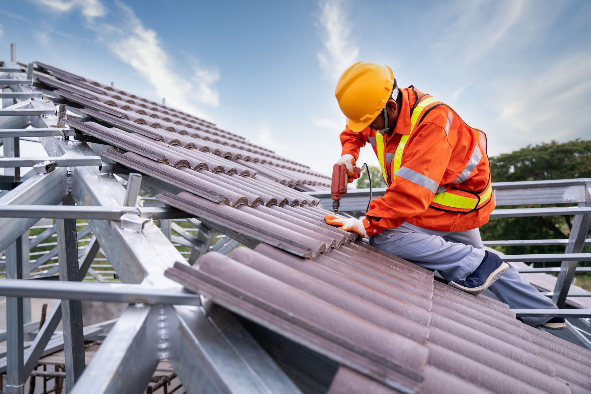 A roofer on steel frame using drill and tools to install tile roof by commercial roofing contractor. A roofer on steel frame using drill and tools to install tile roof by commercial roofing contractor.