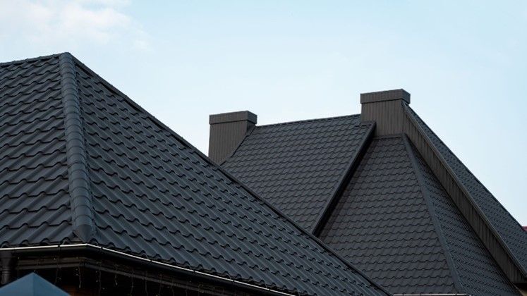 A close-up of modern dark gray metal roofs with chimneys under a clear blue sky, daytime view.