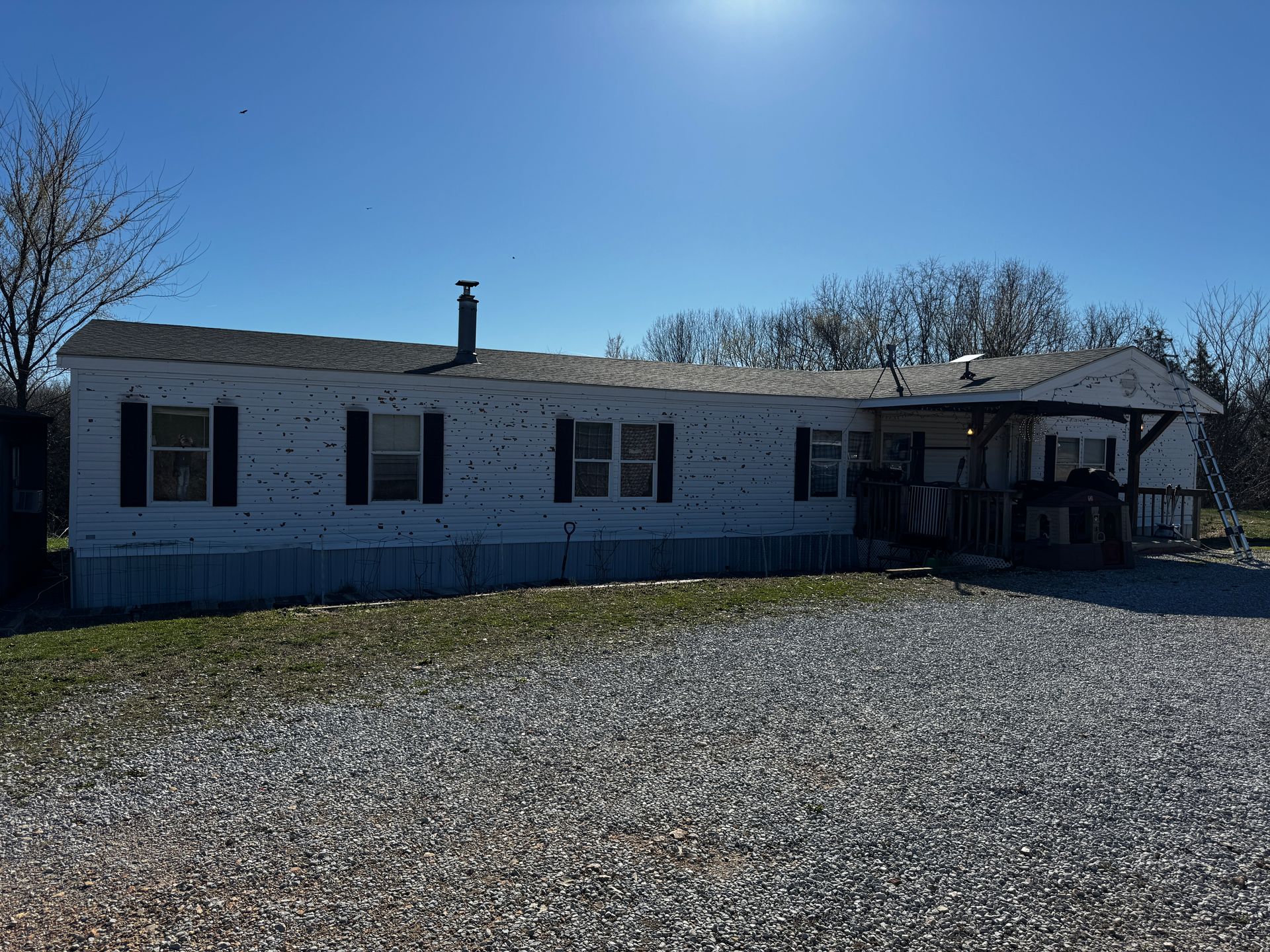 A white mobile home with black shutters is sitting on top of a gravel lot.