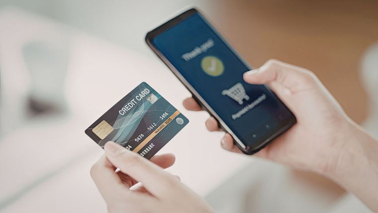 A person holding a dark credit card and a smartphone displaying a successful online shopping payment confirmation.