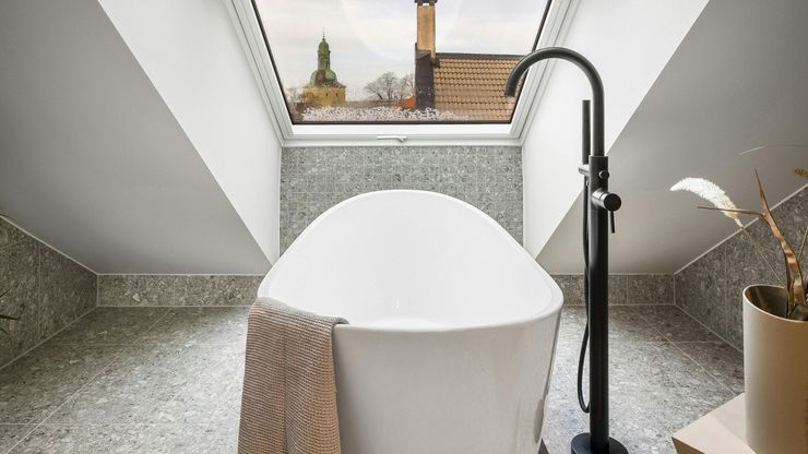 A white freestanding bathtub with a black faucet sits under a skylight with a view of a city skyline.