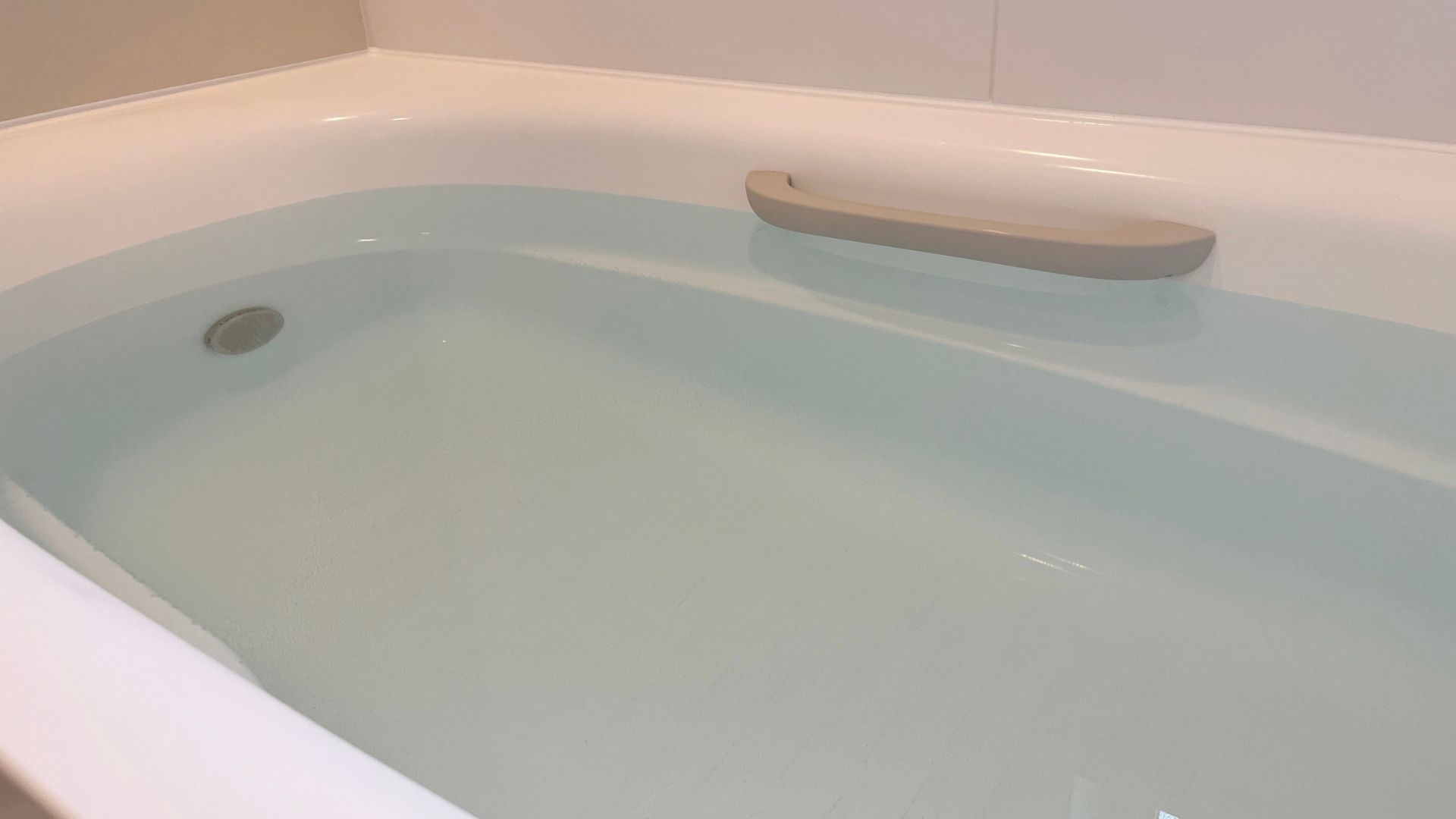 A white bathtub filled with water, featuring a light grey soap dish mounted on the side.