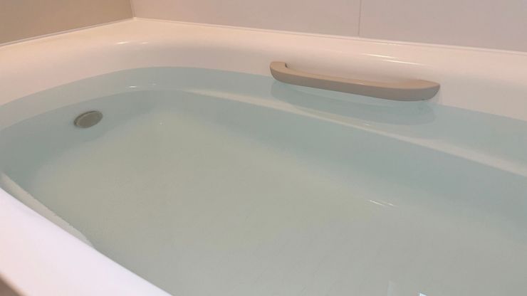 A white bathtub filled with water, featuring a light gray support handle mounted on the inner rim.