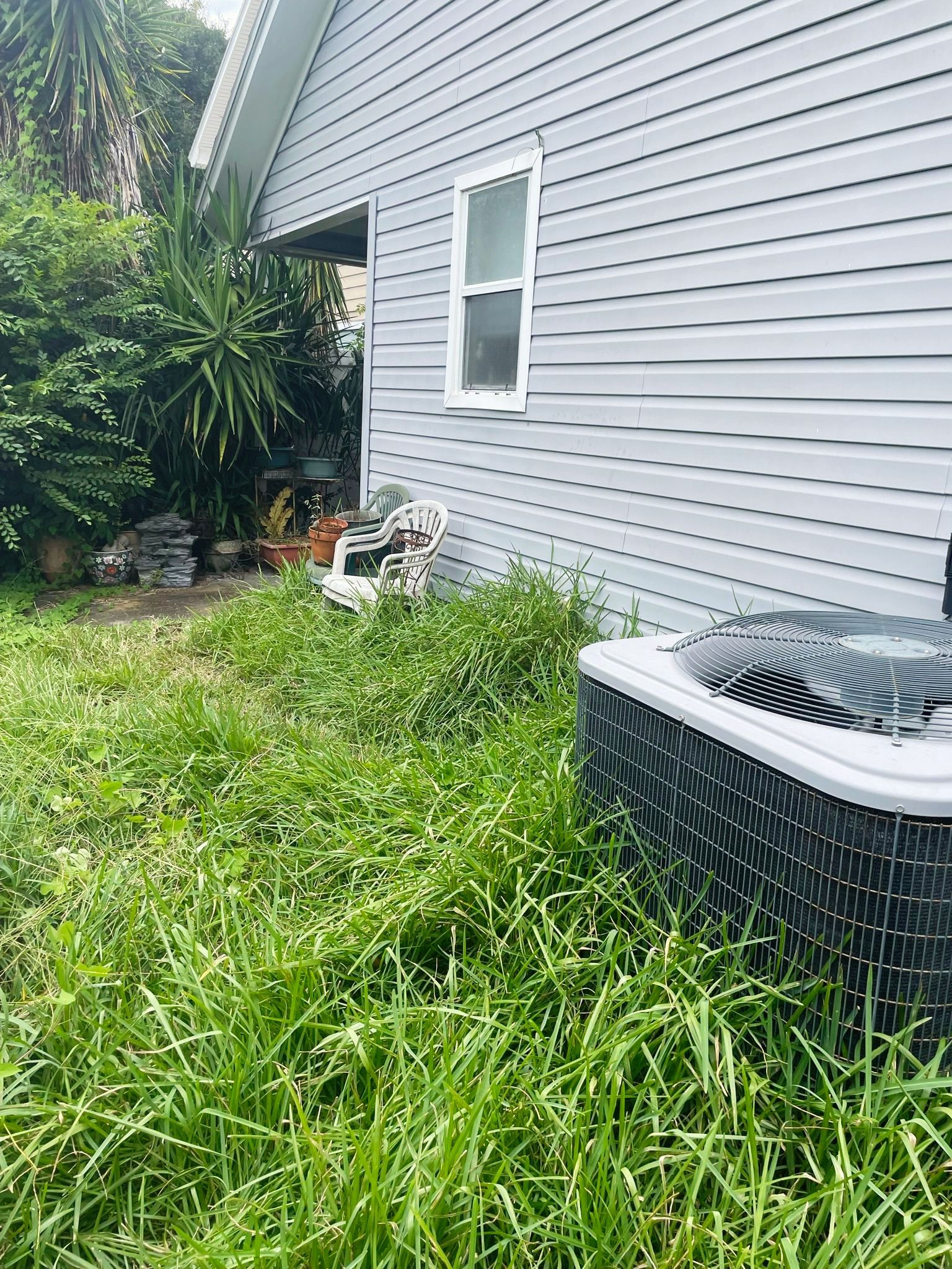 A house with a air conditioner sitting in the grass in front of it.