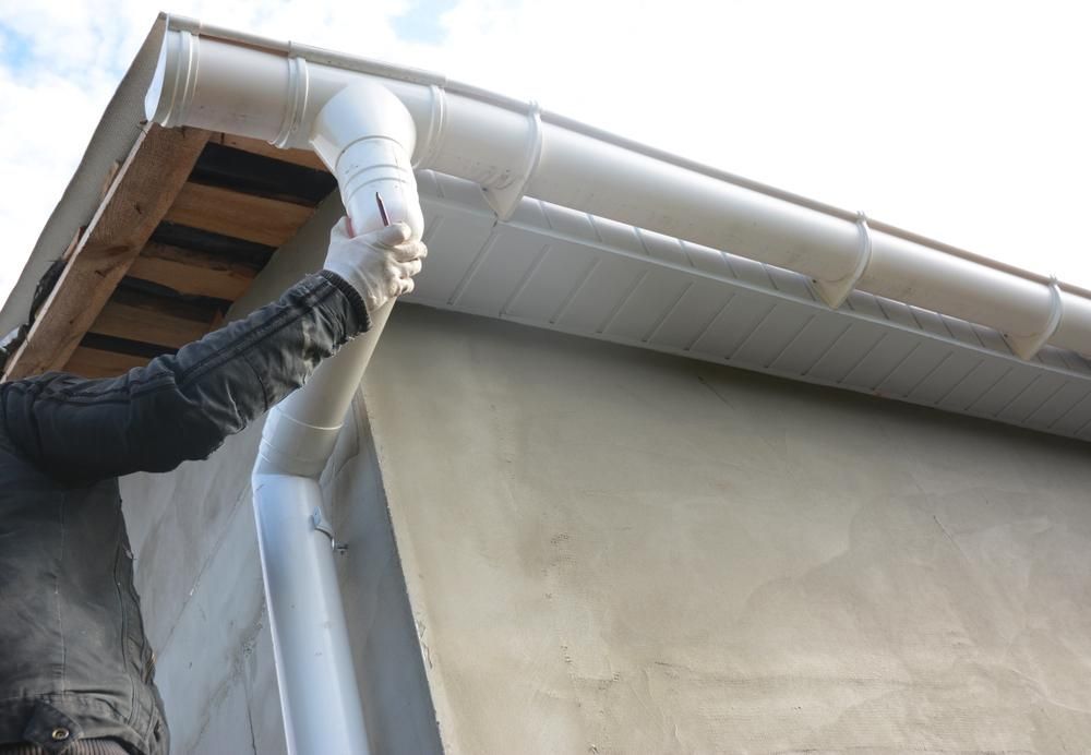 A Man Is Installing a White Gutter — Bradley Roofing in Tuncurry, NSW