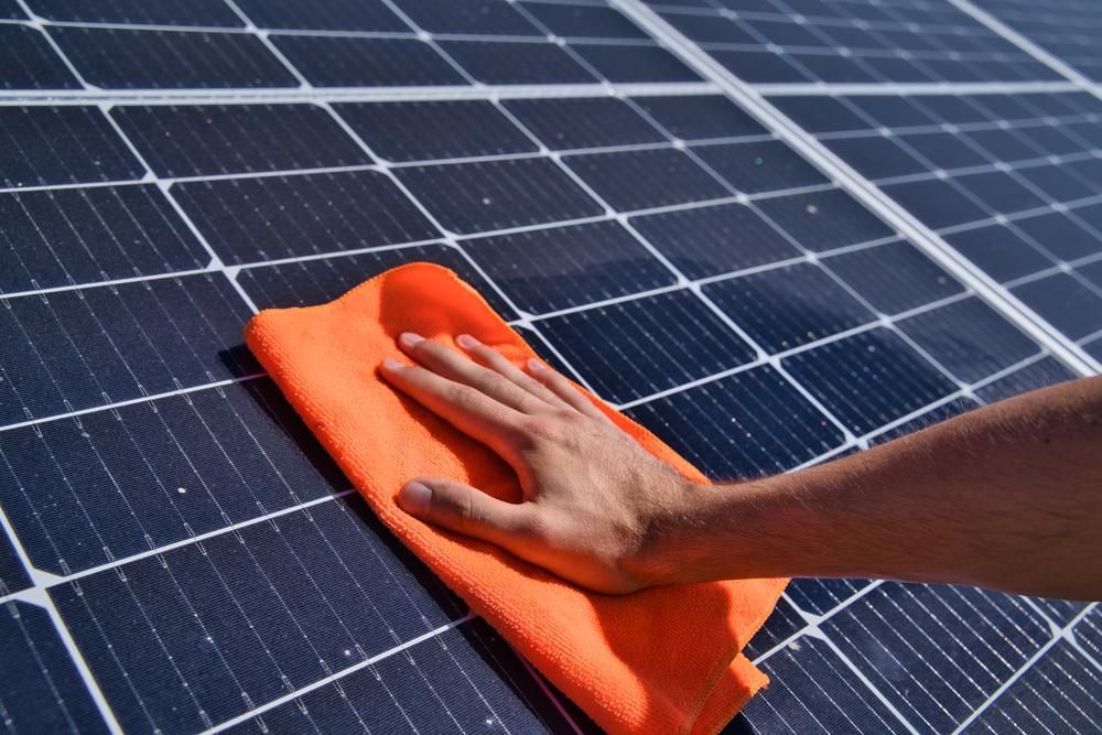 A Person Is Cleaning a Solar Panel with An Orange Cloth — Bradley Roofing in Tuncurry, NSW
