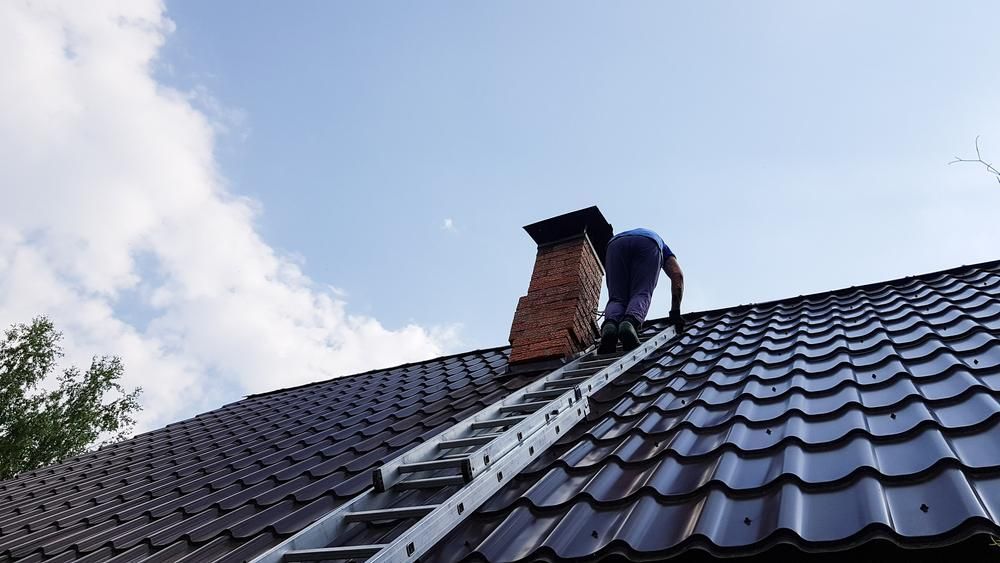 A Man Is Standing on Top of A Roof with A Ladder — Bradley Roofing in Tuncurry, NSW