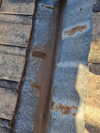 Close-up of a worn, rust-coloured metal roof valley. Shingles flank a channel showing water stains. — Bradley Roofing in Tuncurry, NSW