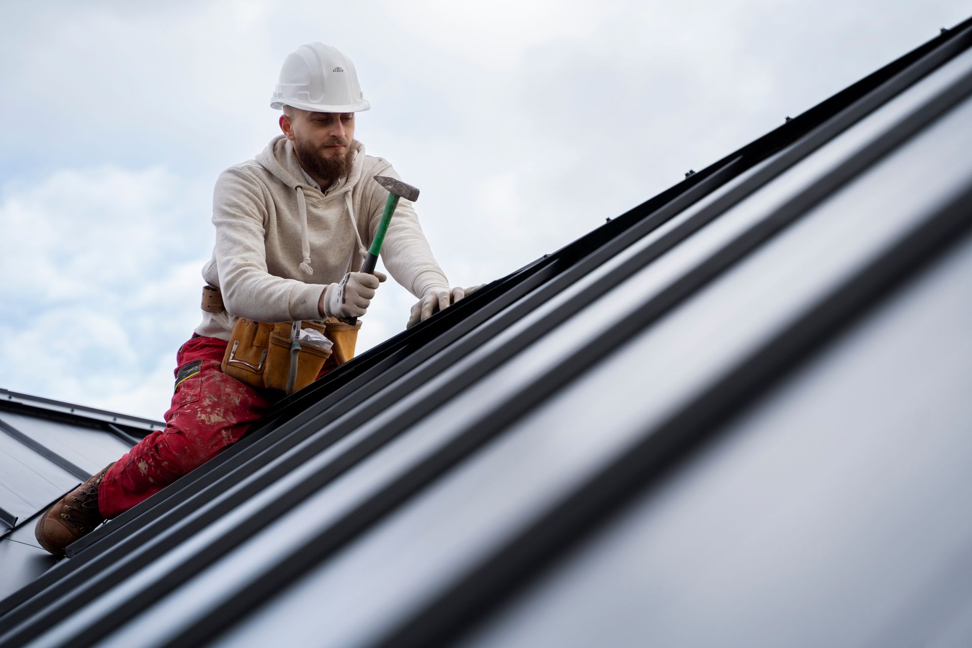 Roofer in hard hat hammering metal roofing on a cloudy day. — Bradley Roofing in Tuncurry, NSW