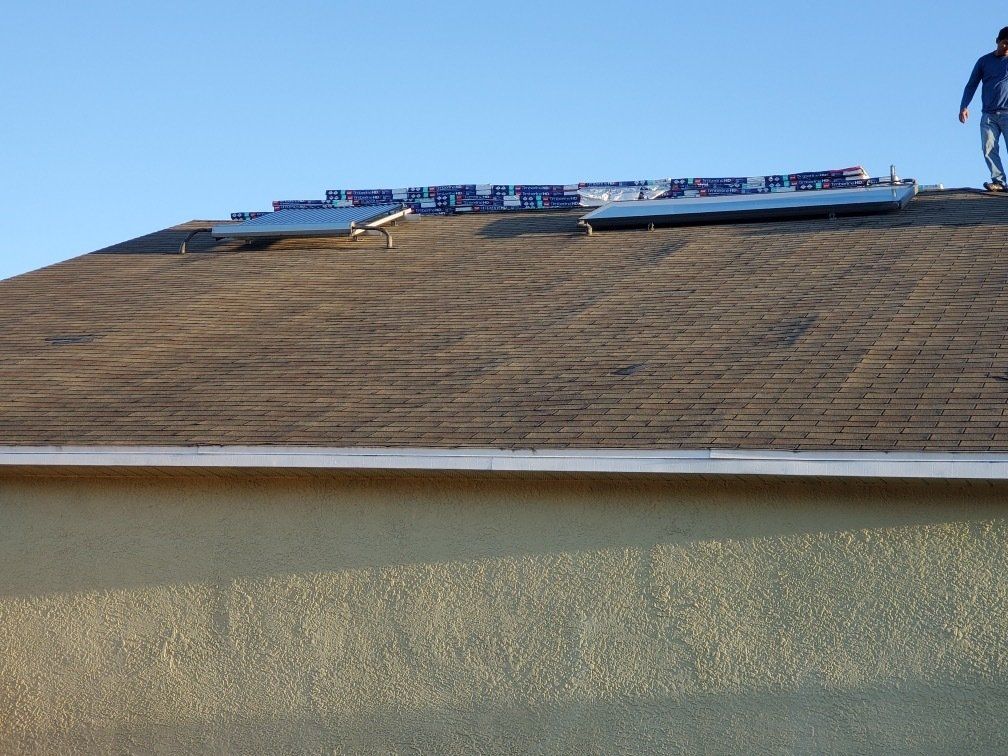 A man standing on top of a roof with shingles on it