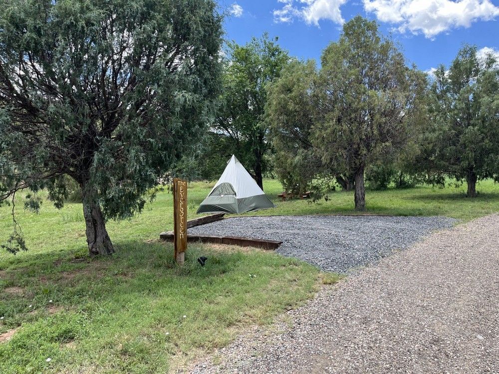 A campsite with a tent, gravel, trees, and a sign post on a sunny day.