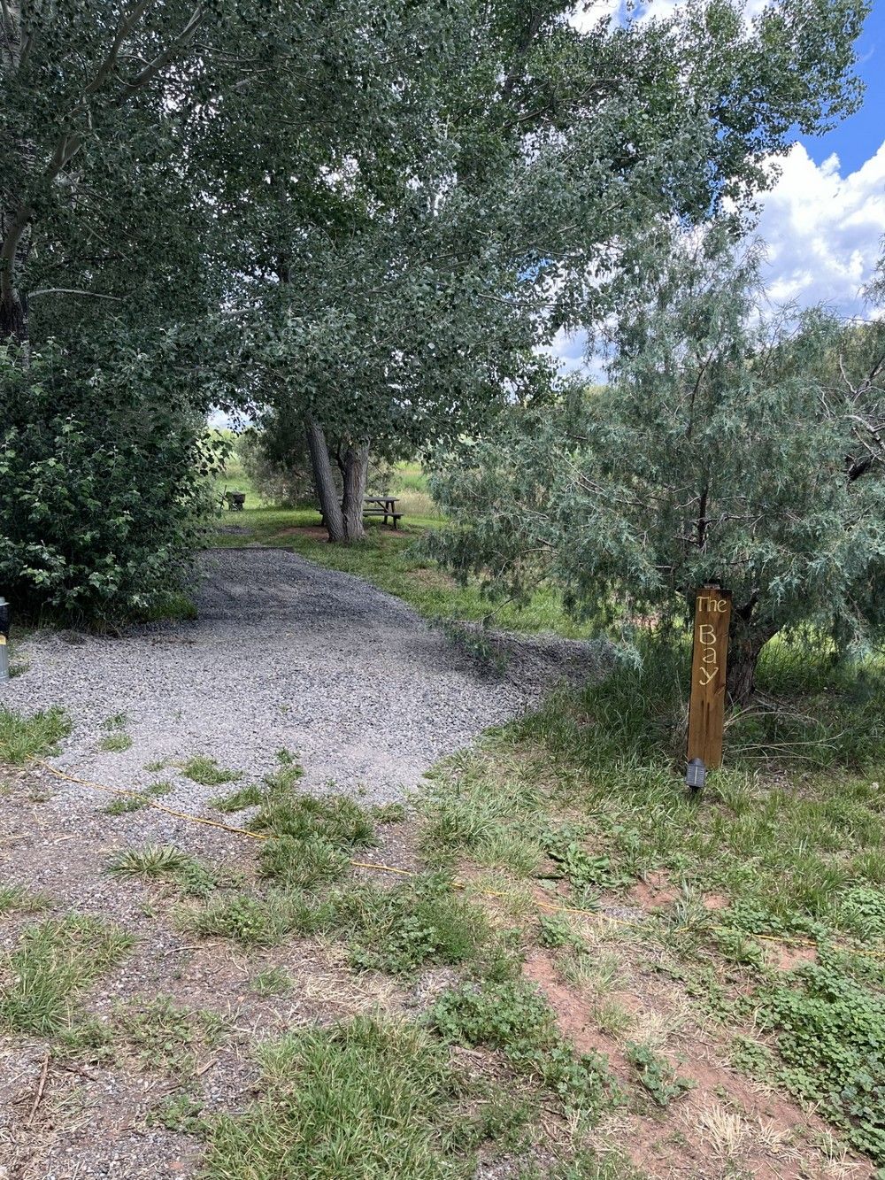 Gravel path leading into a shaded area with trees. A wooden post is visible.