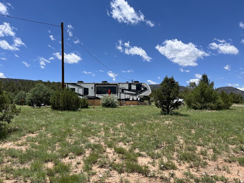RV parked in grassy field with a blue sky and scattered clouds. Tall utility pole in the frame.