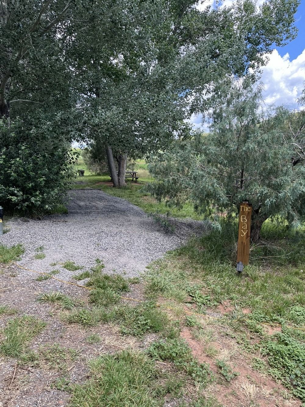 Gravel path leads to trees and a distant bench in a green outdoor area. A wooden post is on the right.