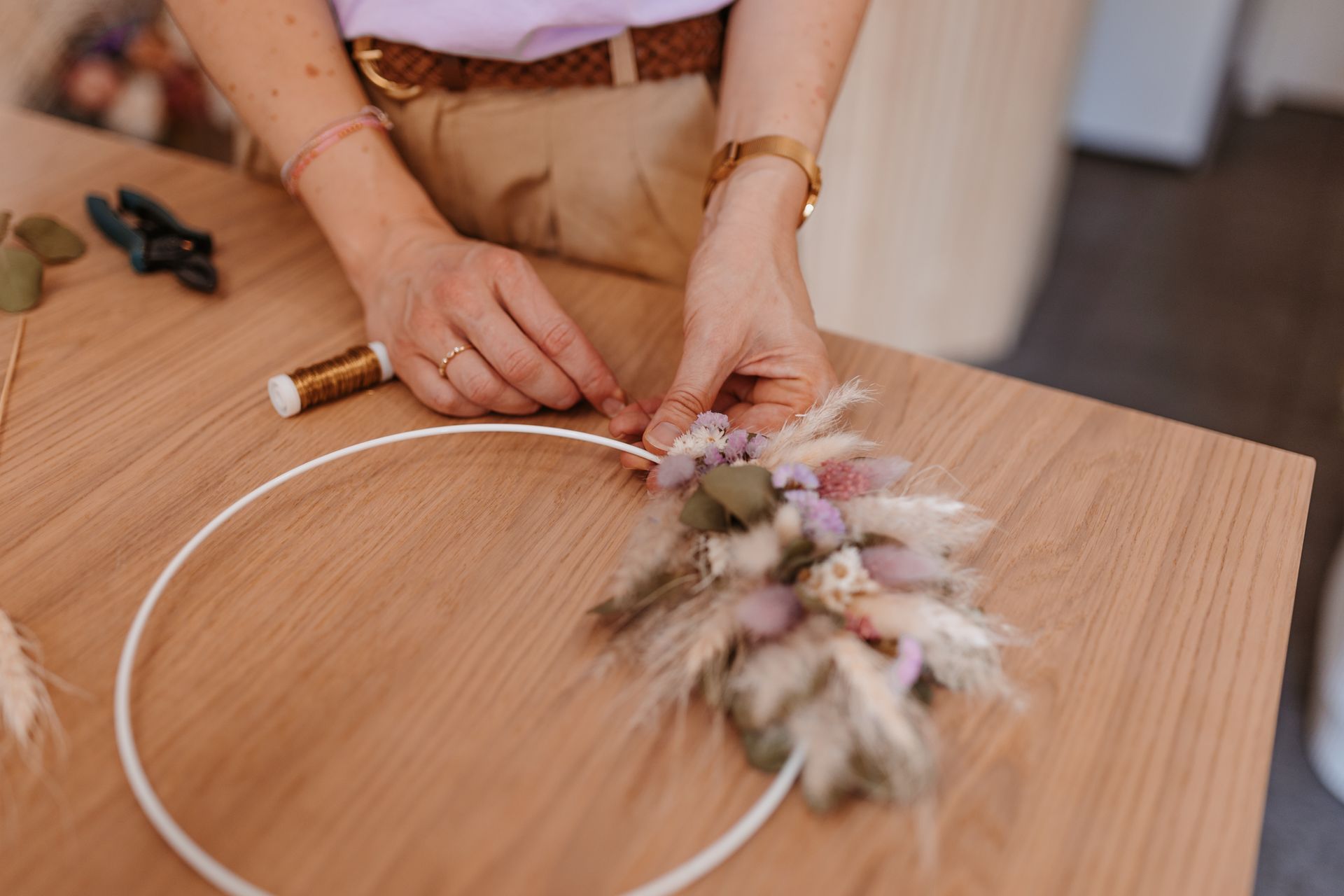 A woman is making a wreath with dried flowers on a wooden table.