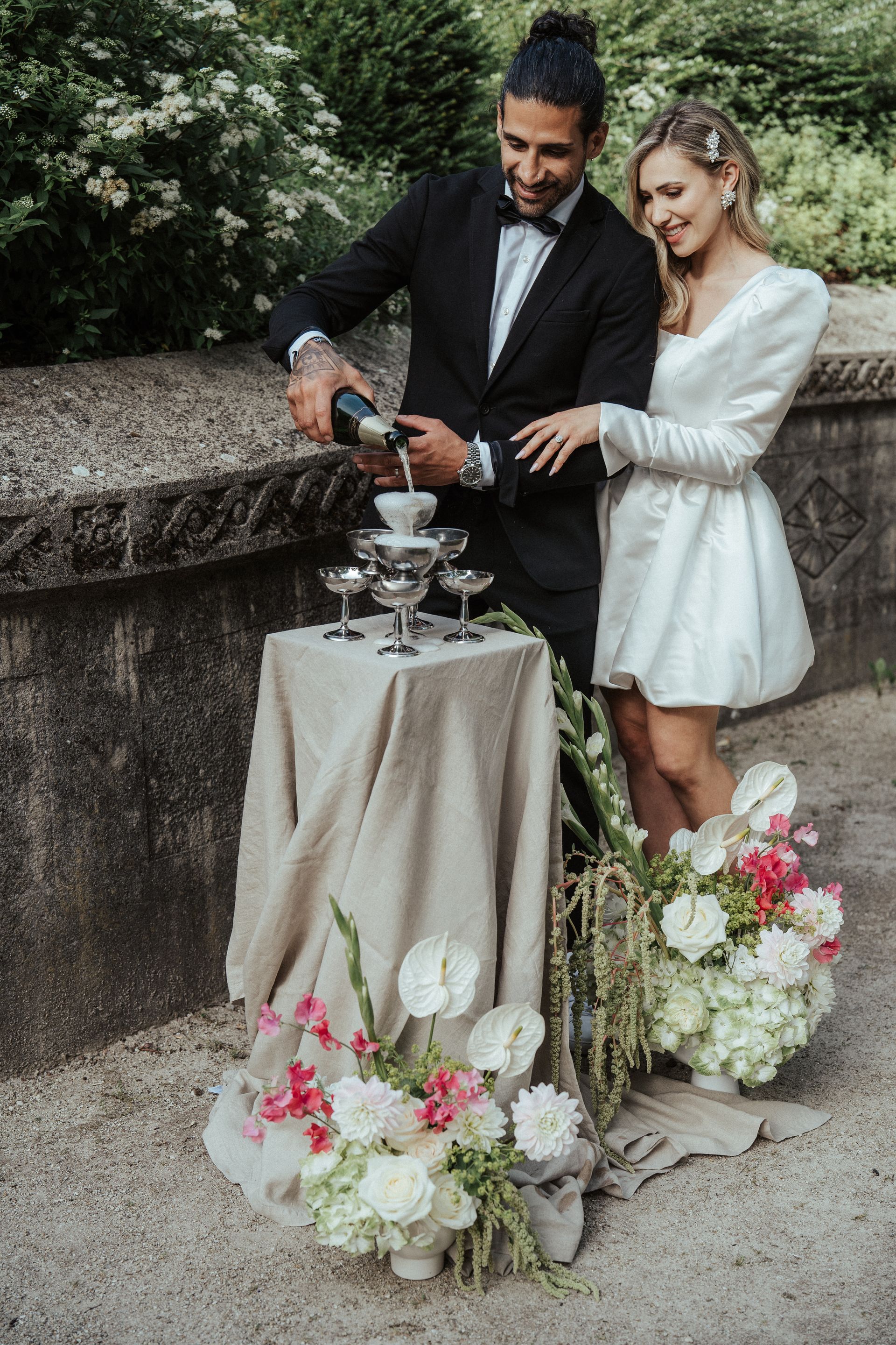 A bride and groom are pouring champagne on a table.