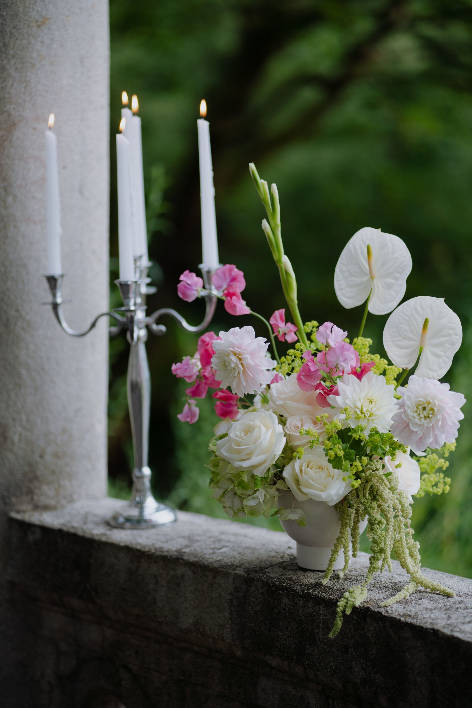 A vase filled with pink and white flowers and candles on a balcony.
