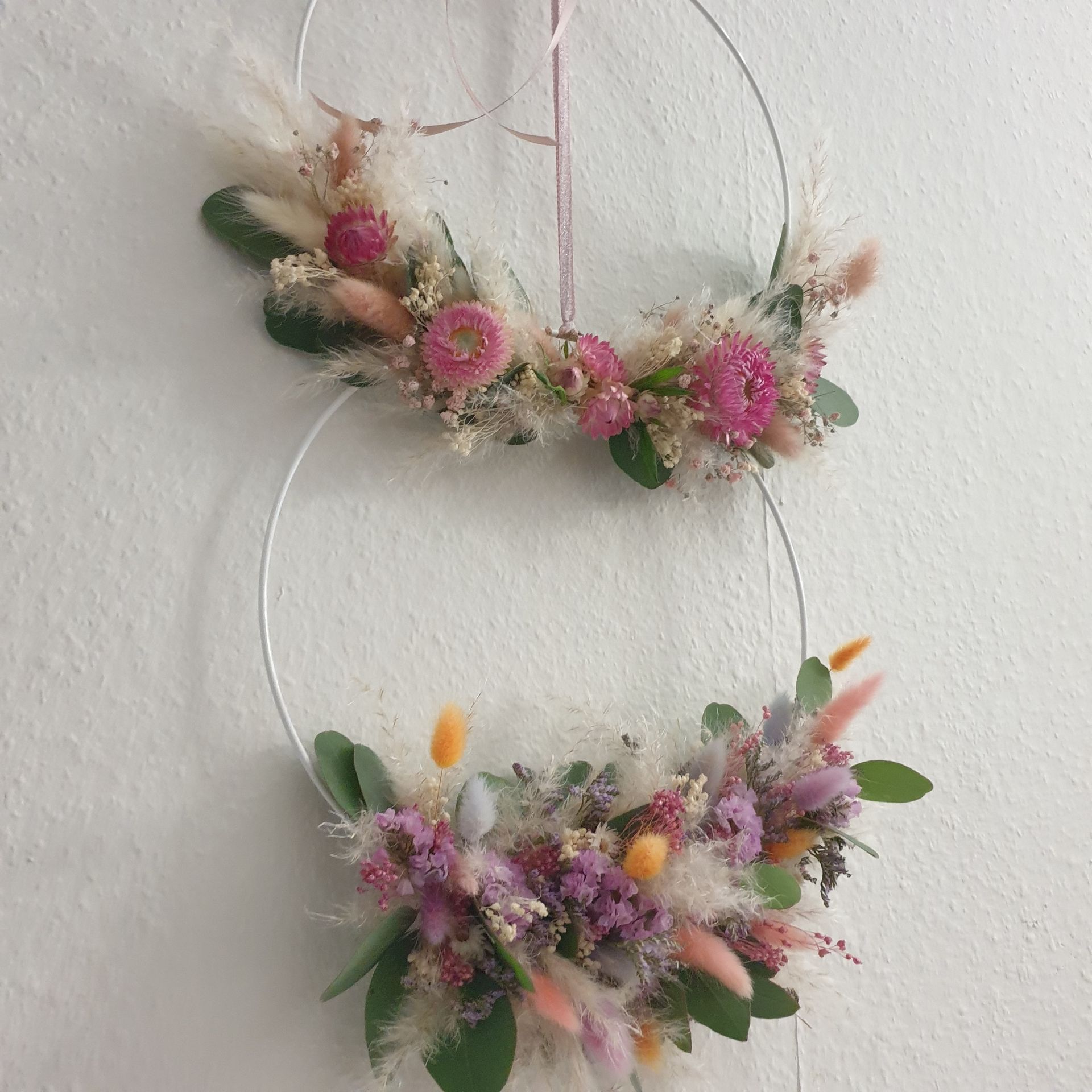 Two wreaths with pink and purple flowers hanging on a white wall