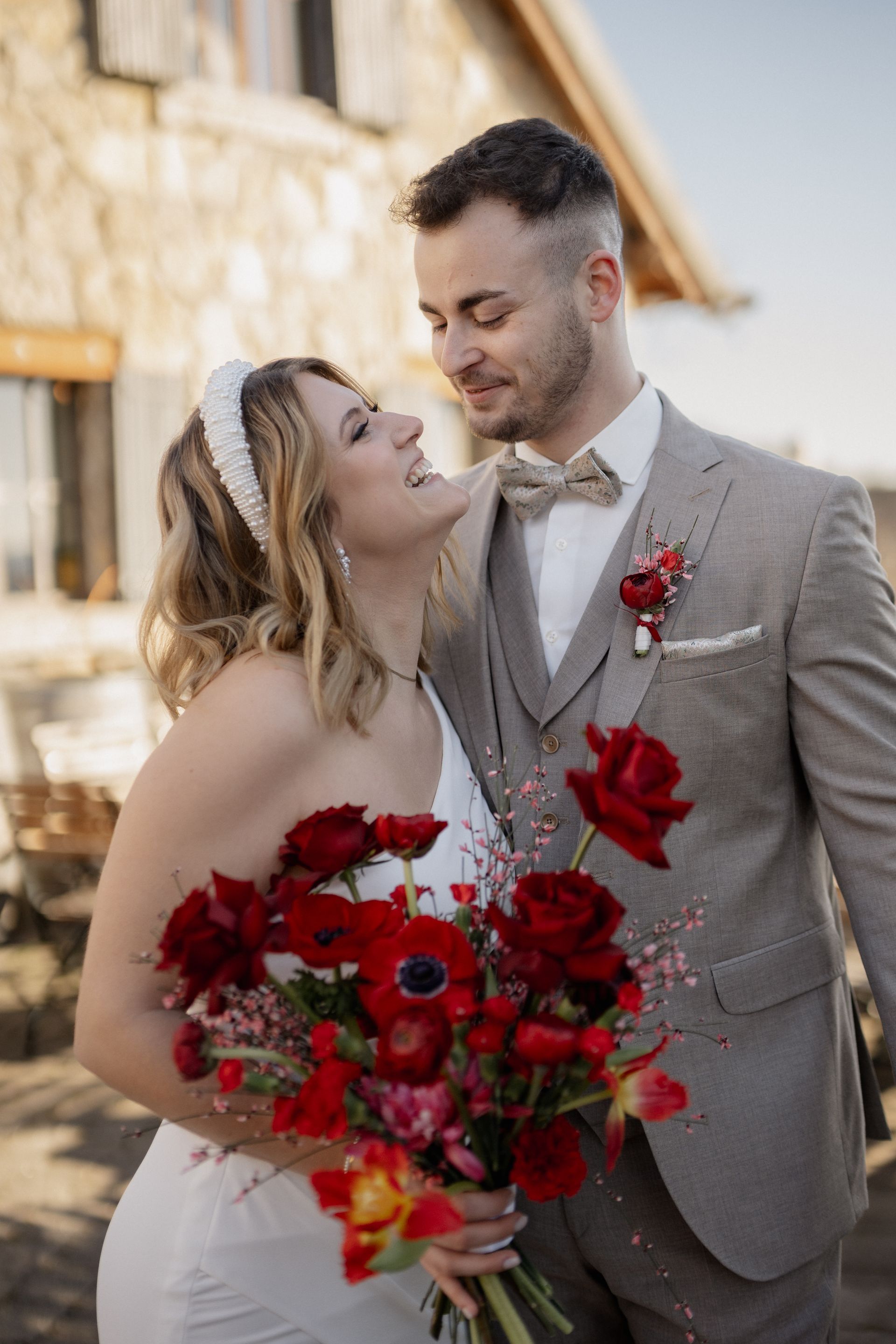 A bride and groom are posing for a picture while the bride is holding a bouquet of red flowers.