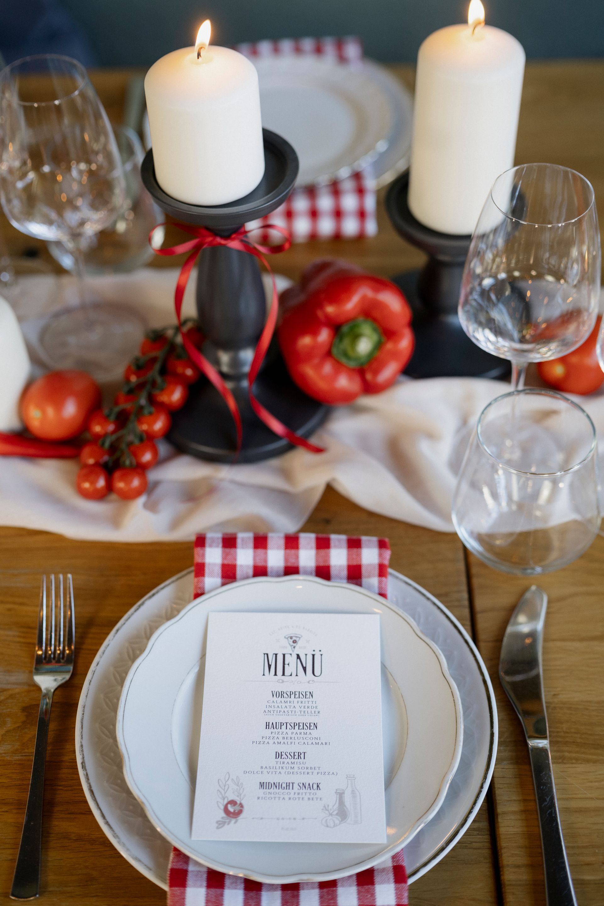 A table setting with plates , candles , wine glasses and vegetables.