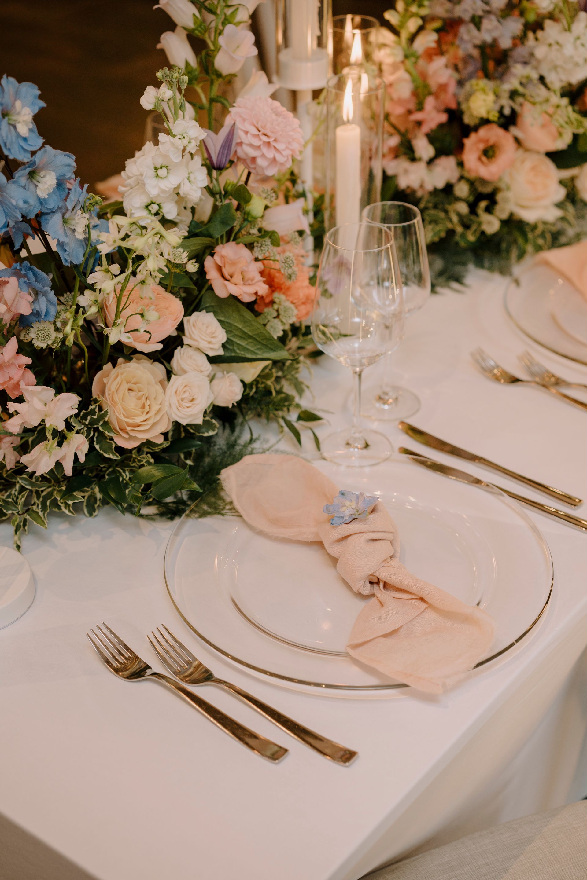 A table set for a wedding reception with plates , silverware , candles and flowers.
