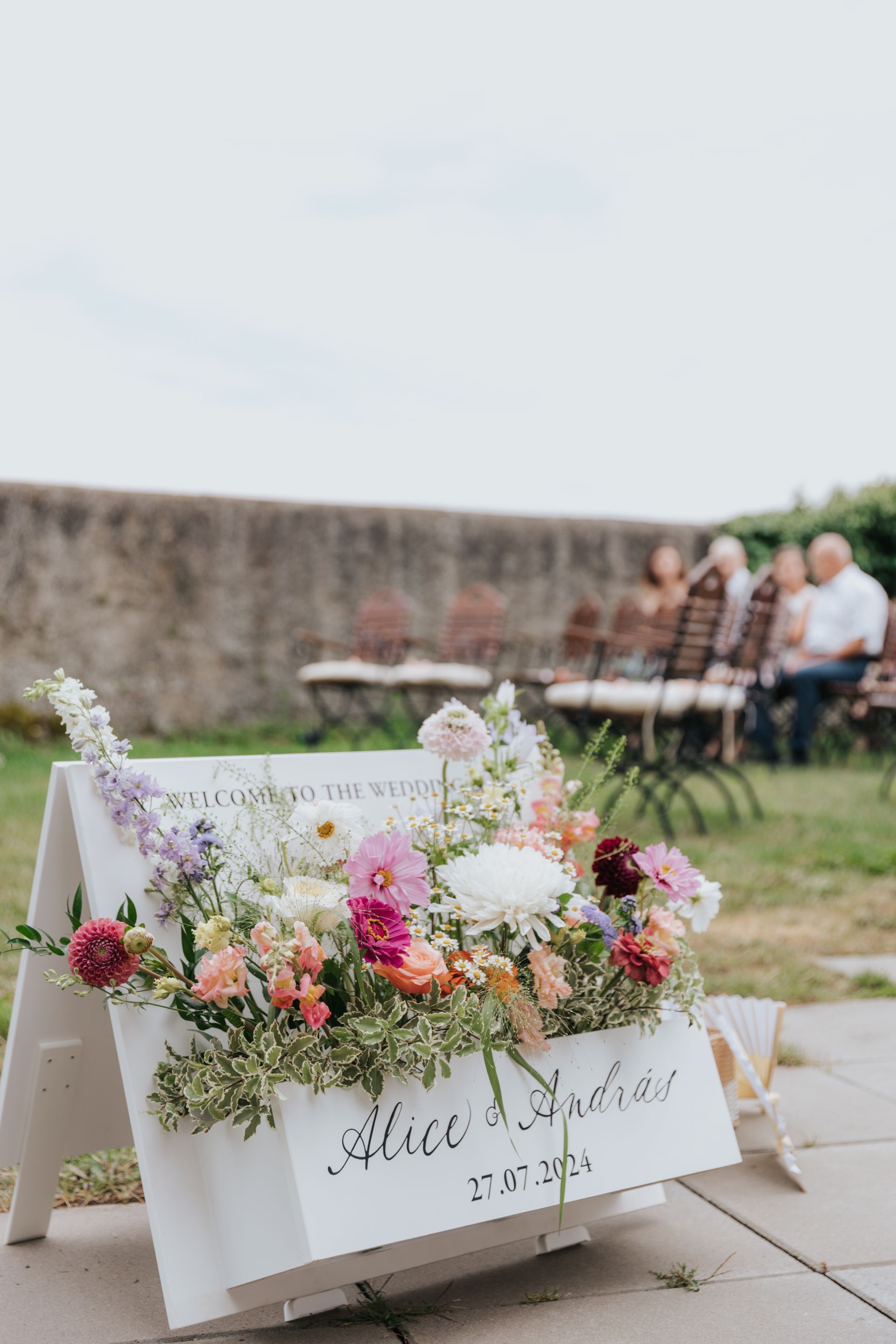 A sign with flowers on it is sitting on a sidewalk.