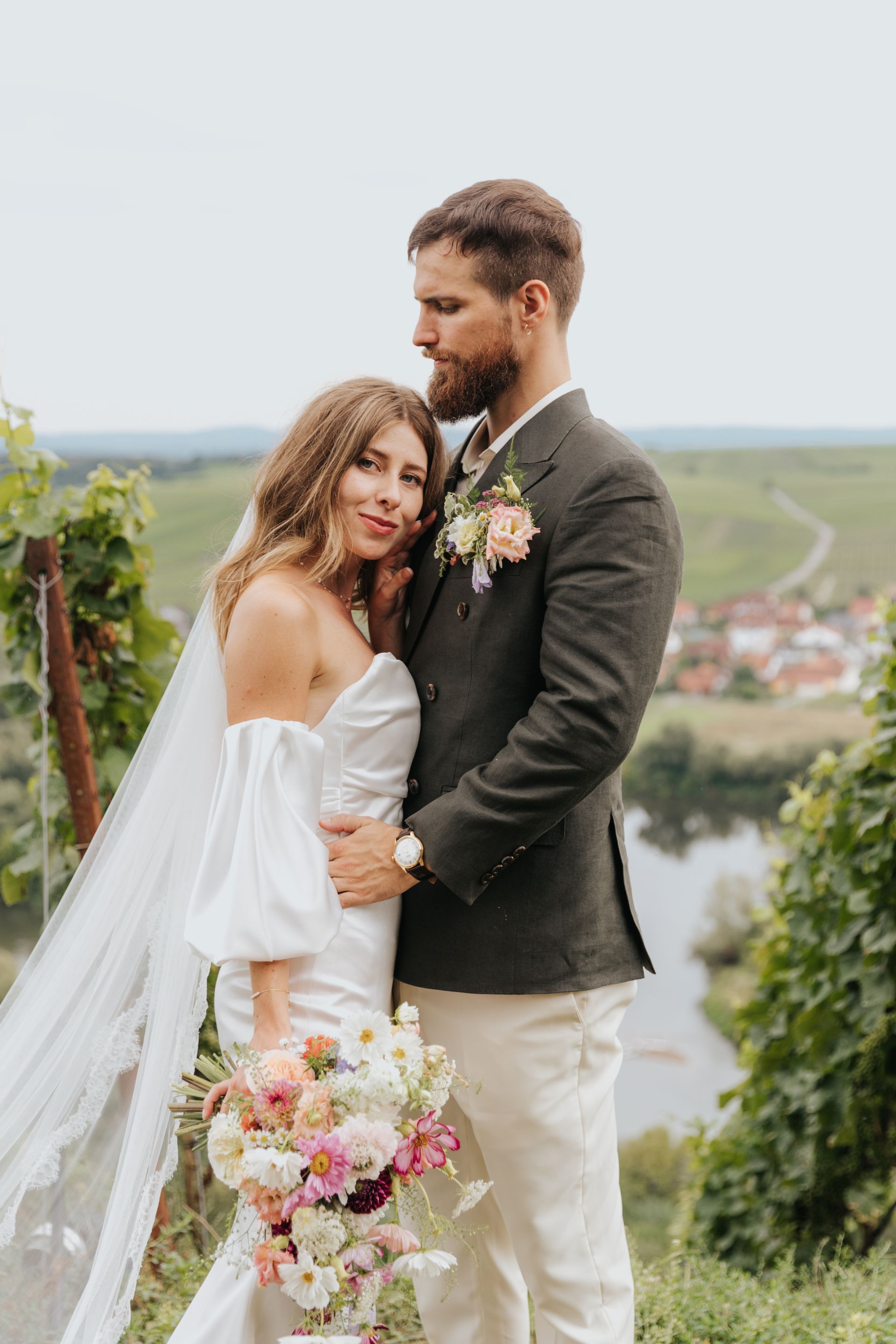 A bride and groom are posing for a picture in a vineyard.