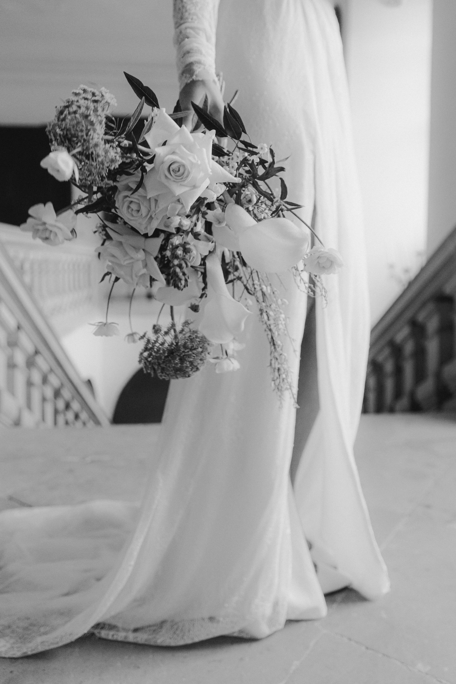 A black and white photo of a bride in a wedding dress holding a bouquet of flowers.
