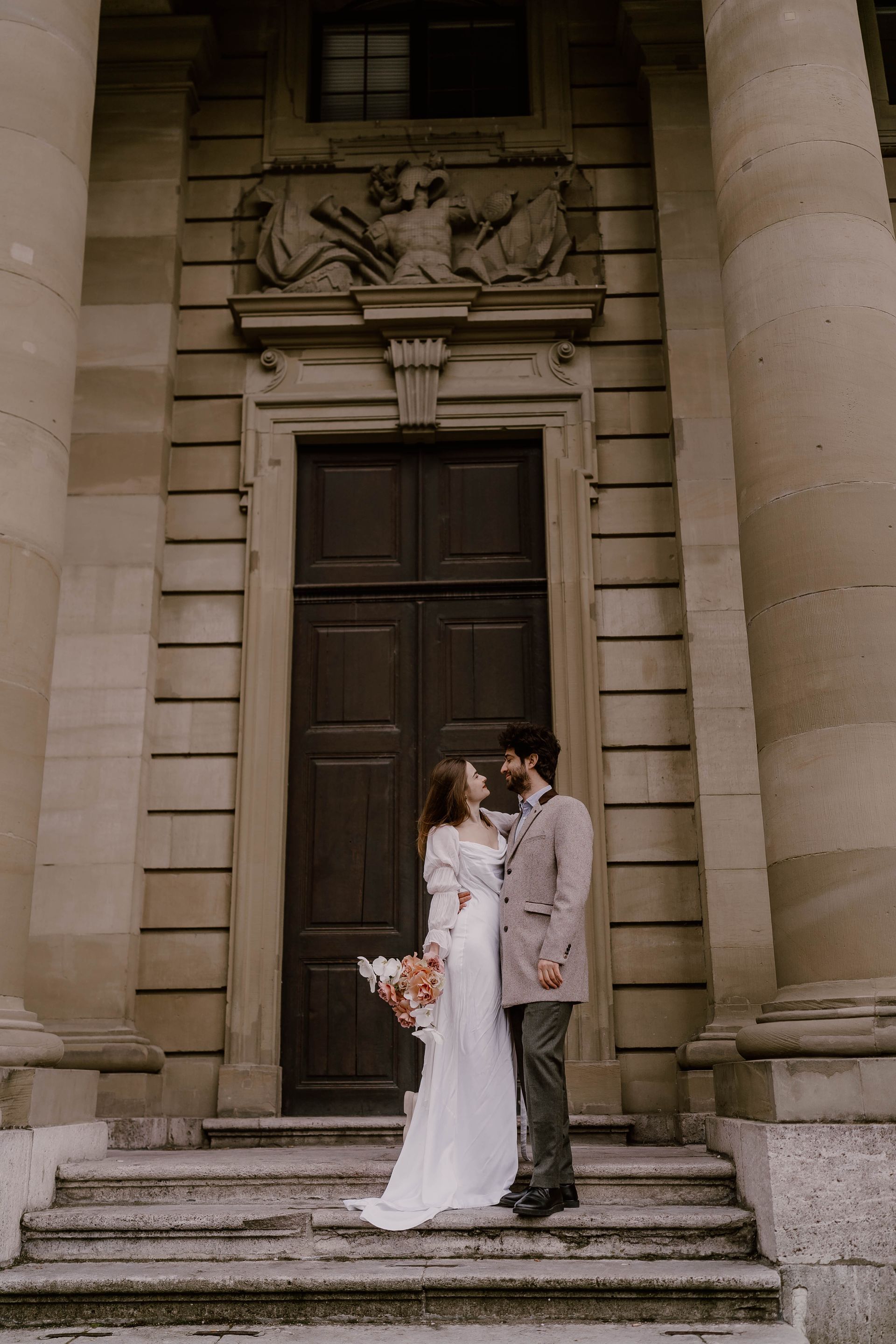 A bride and groom are standing on the steps of a building.