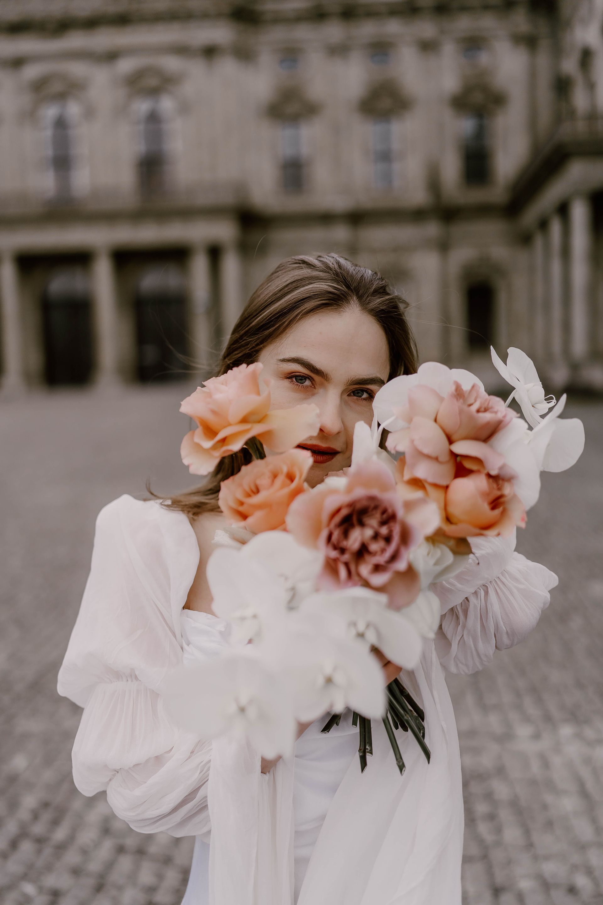 A woman in a white dress is holding a bouquet of flowers in front of her face.