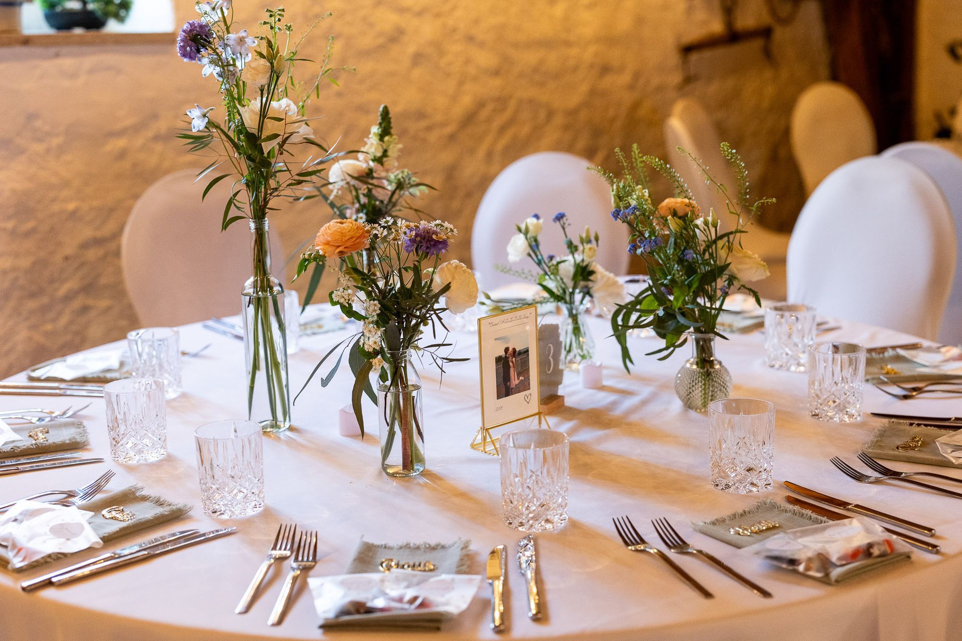 A table set for a wedding reception with flowers in vases on it.