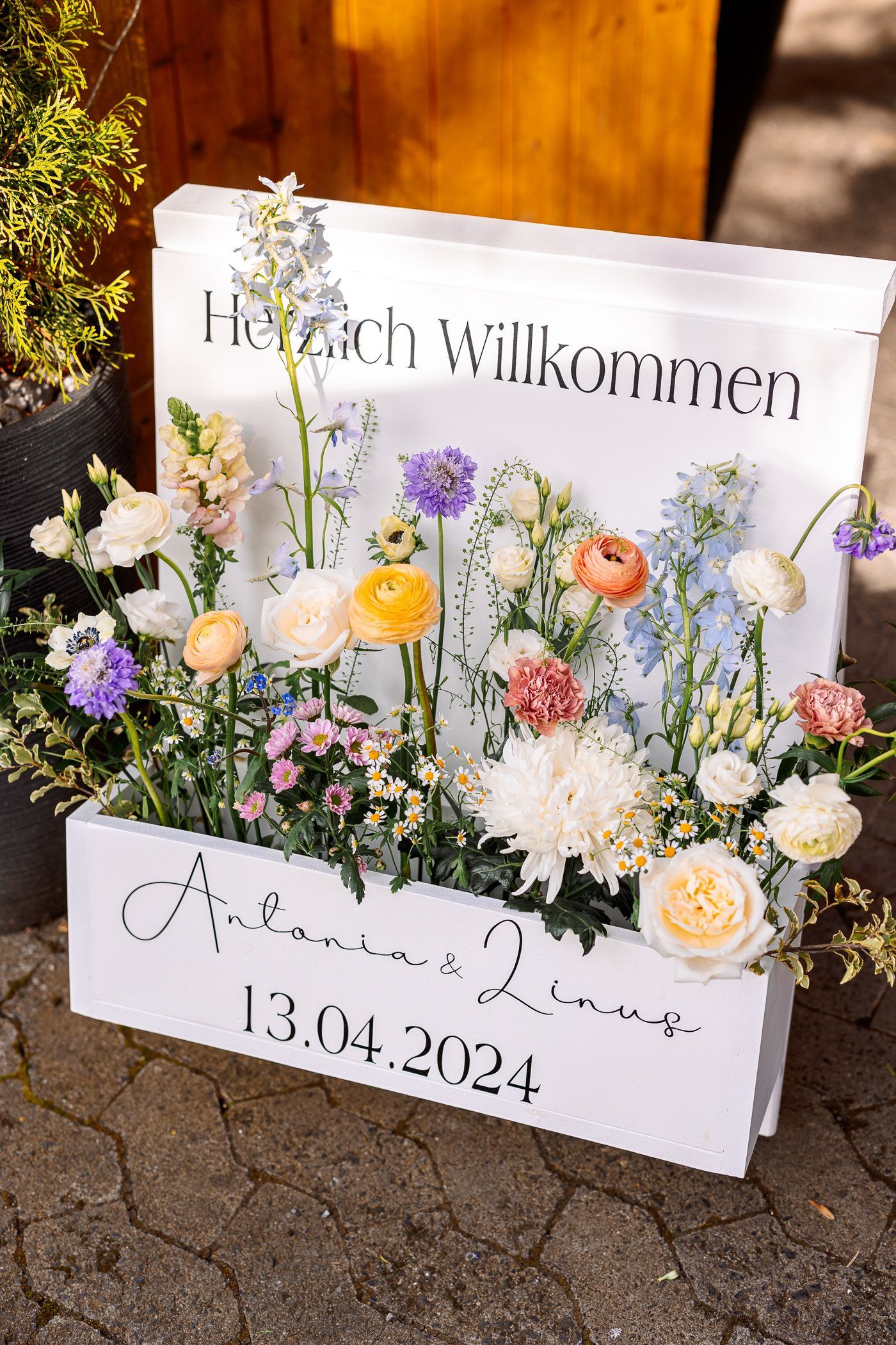 A sign with flowers on it is sitting on a sidewalk.