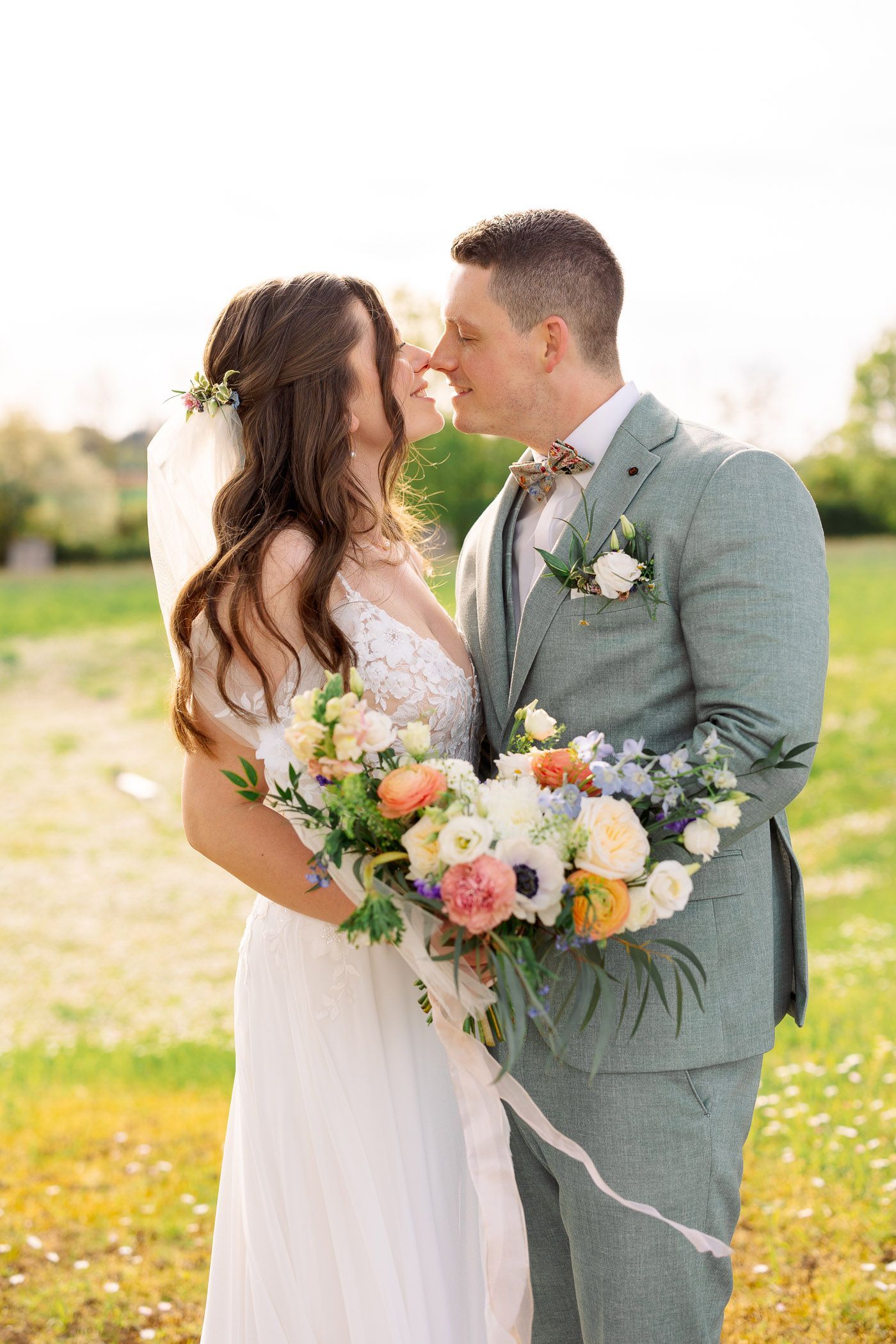 A bride and groom are kissing in a field while holding a bouquet of flowers.