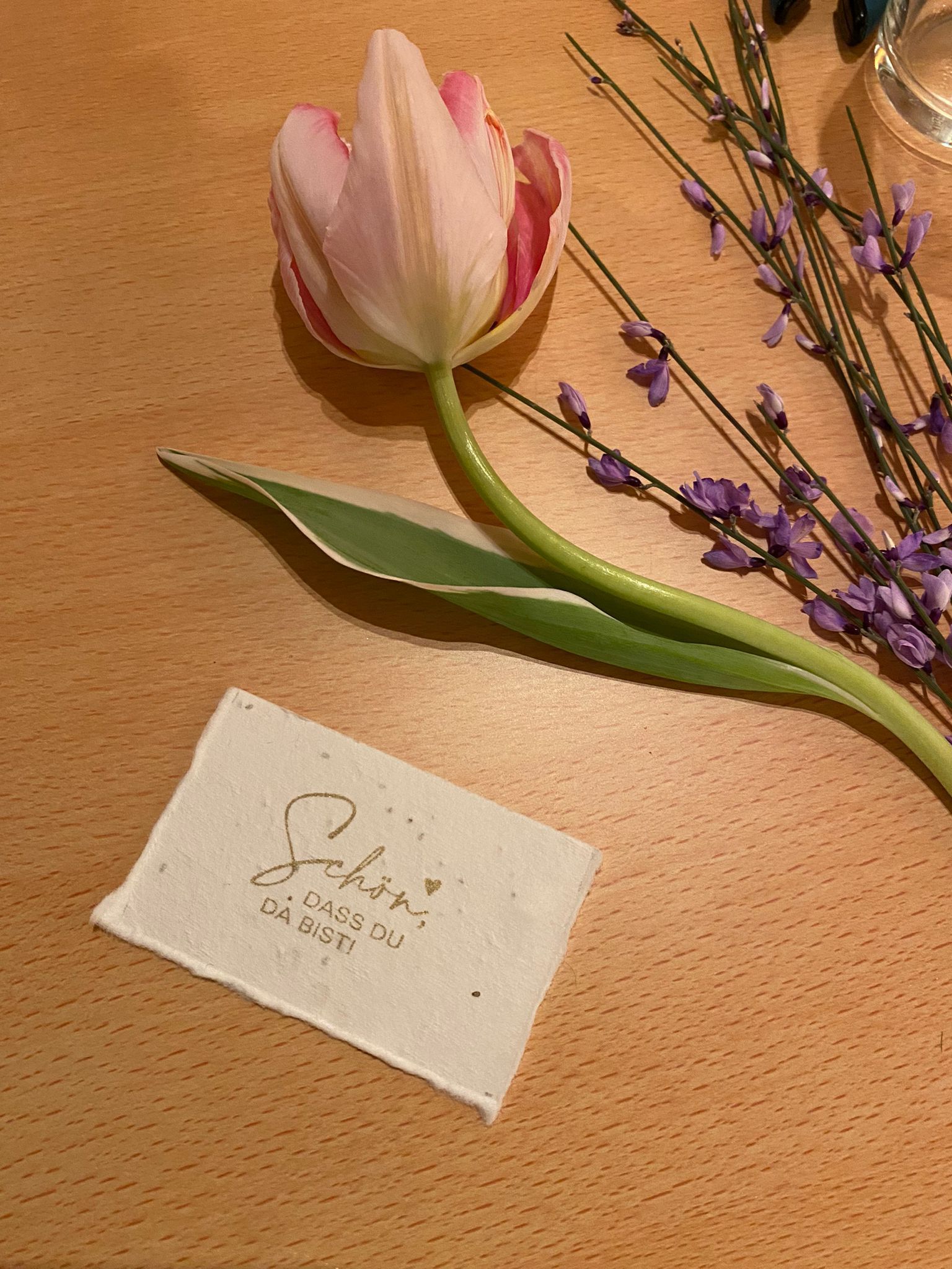 A pink tulip is sitting on a wooden table next to a note.