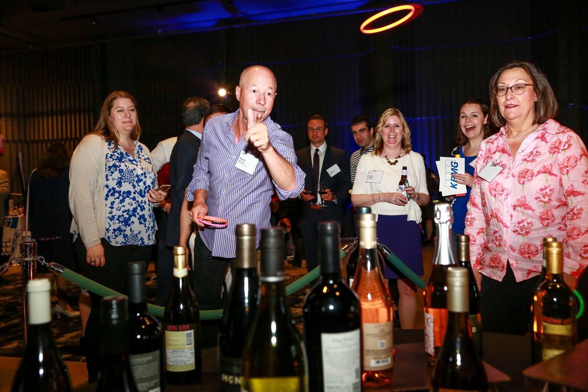 A group of people are standing around a table with bottles of wine.