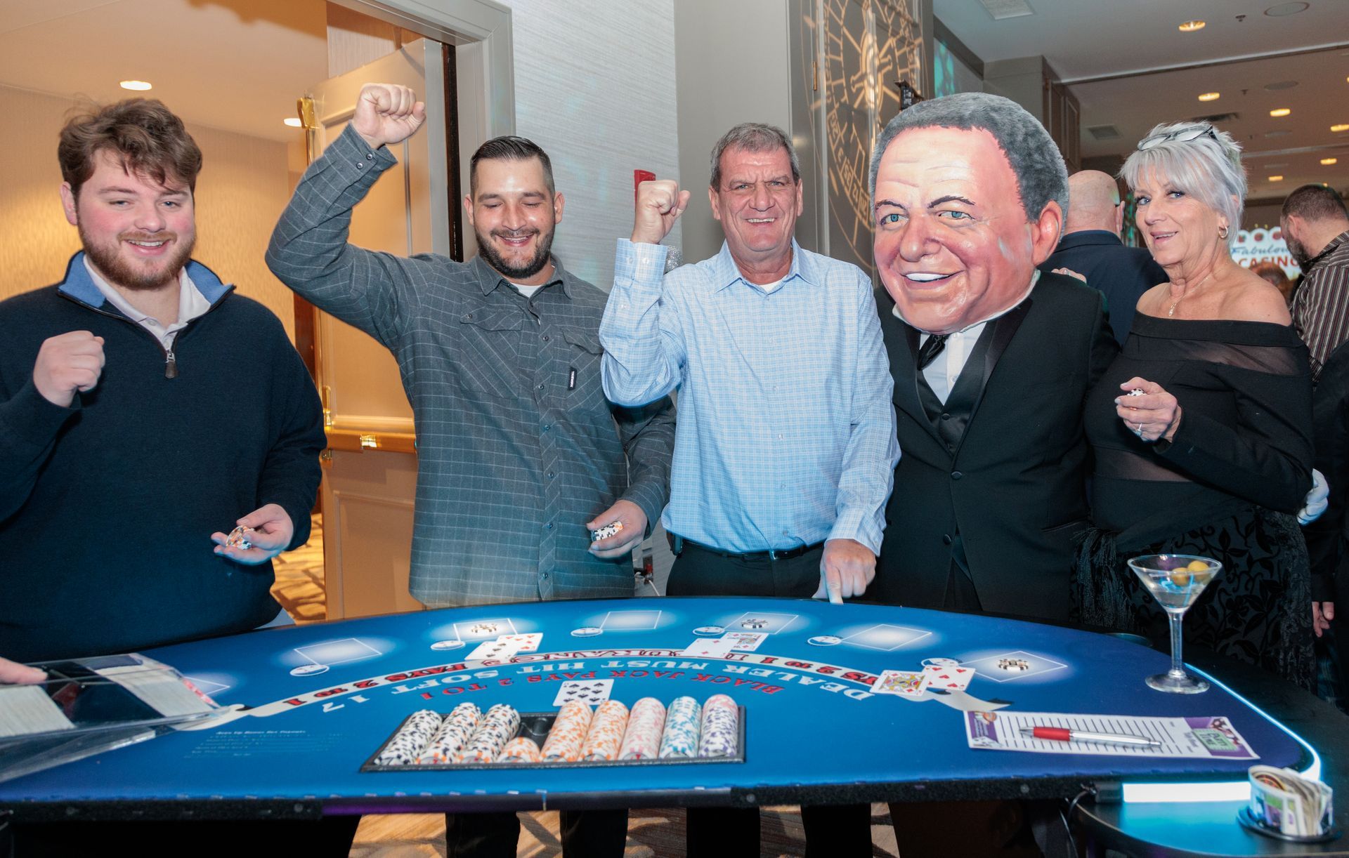 A group of people are standing around a poker table.