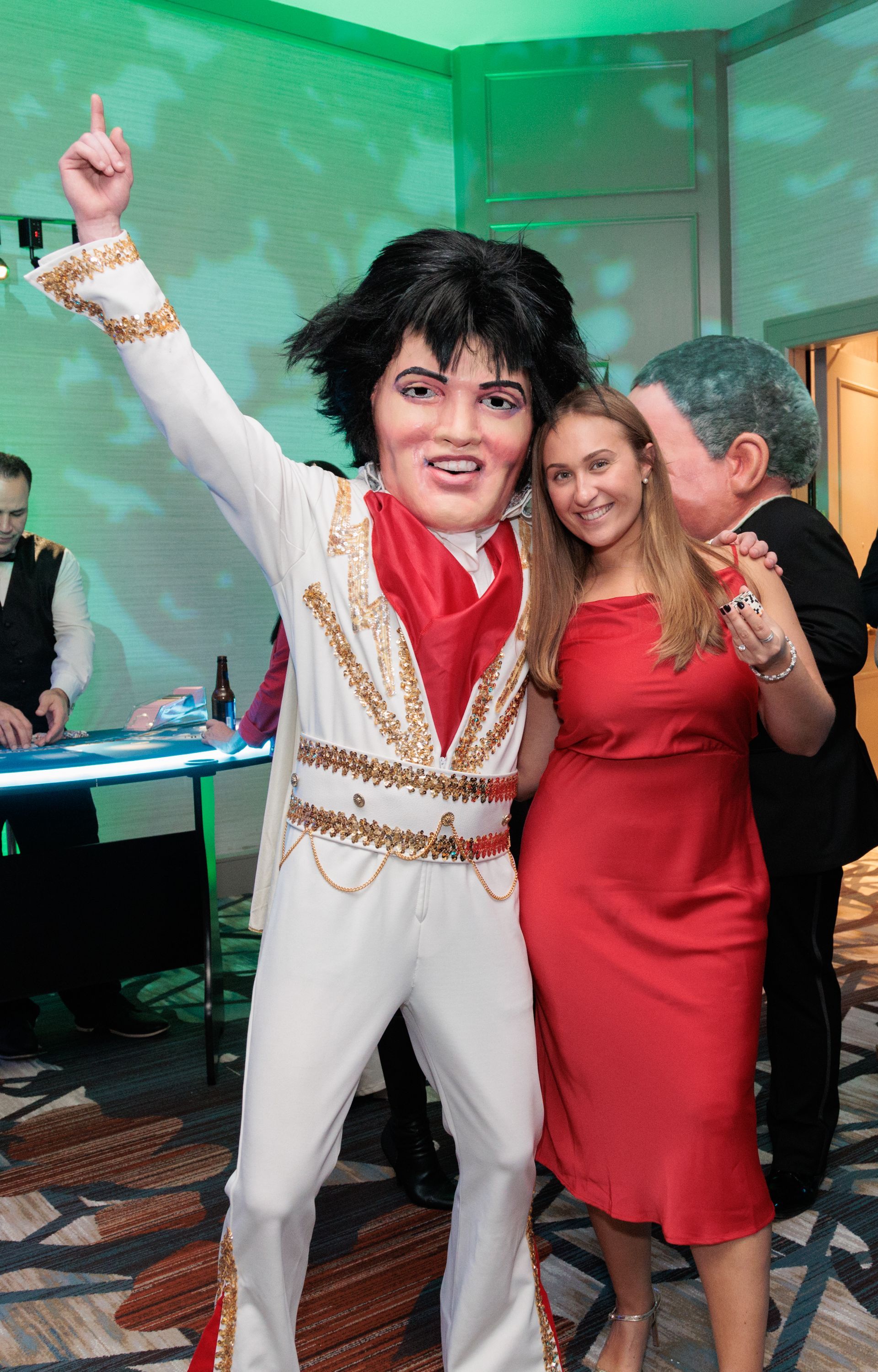 A woman in a red dress is standing next to a mascot dressed as elvis presley.