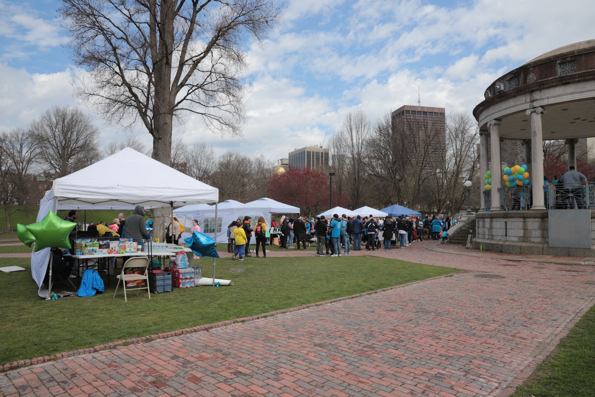A group of people are gathered in a park with tents and balloons.