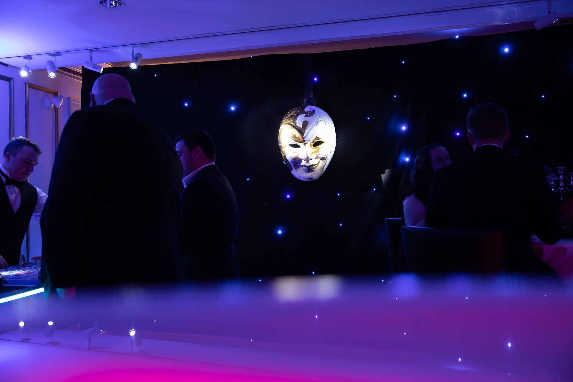 A group of people are standing in a dark room with a mask on the wall.