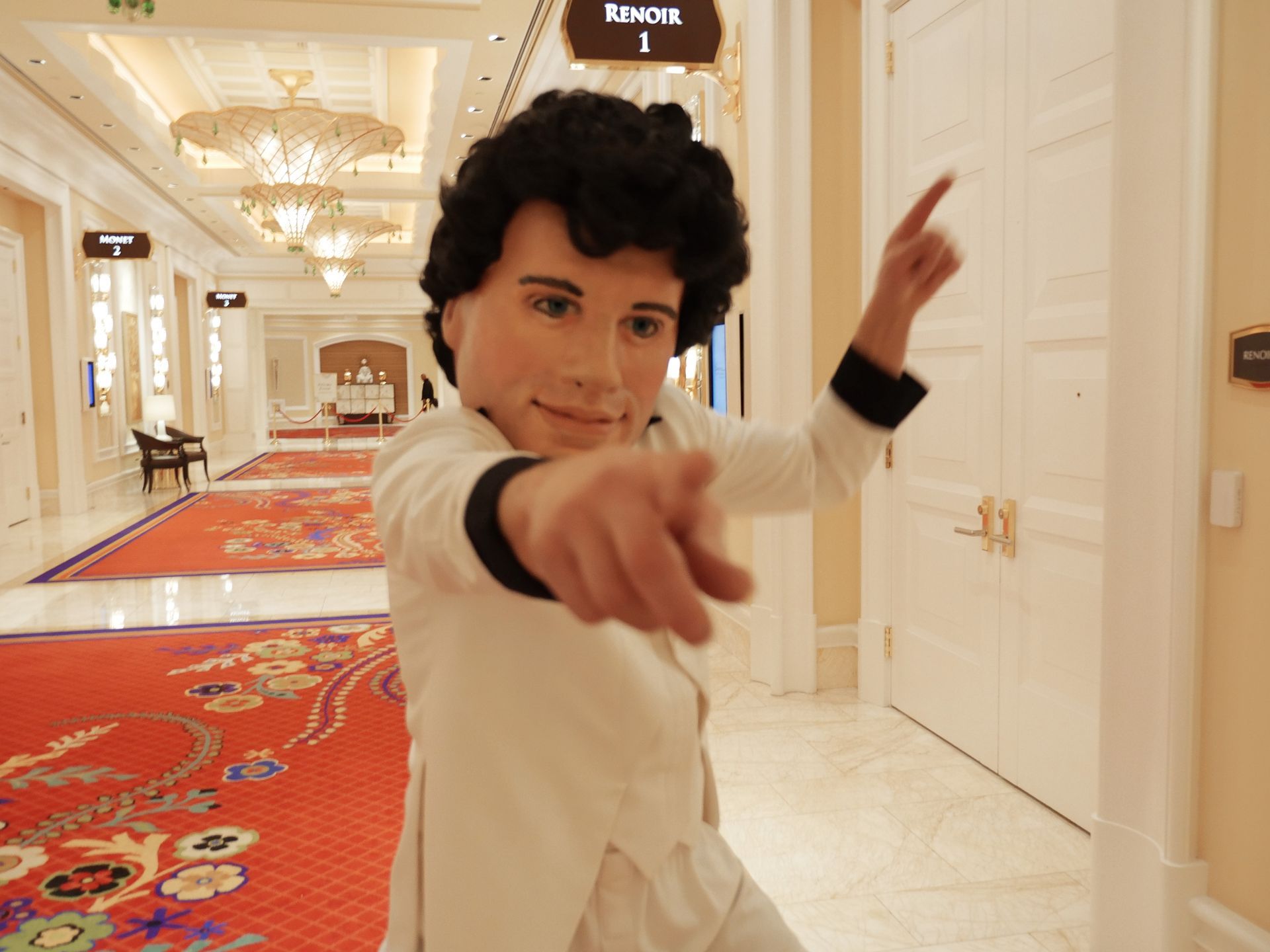 A man in a white suit is pointing at the camera