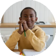 A young boy is sitting at a table with a pencil in his hand.