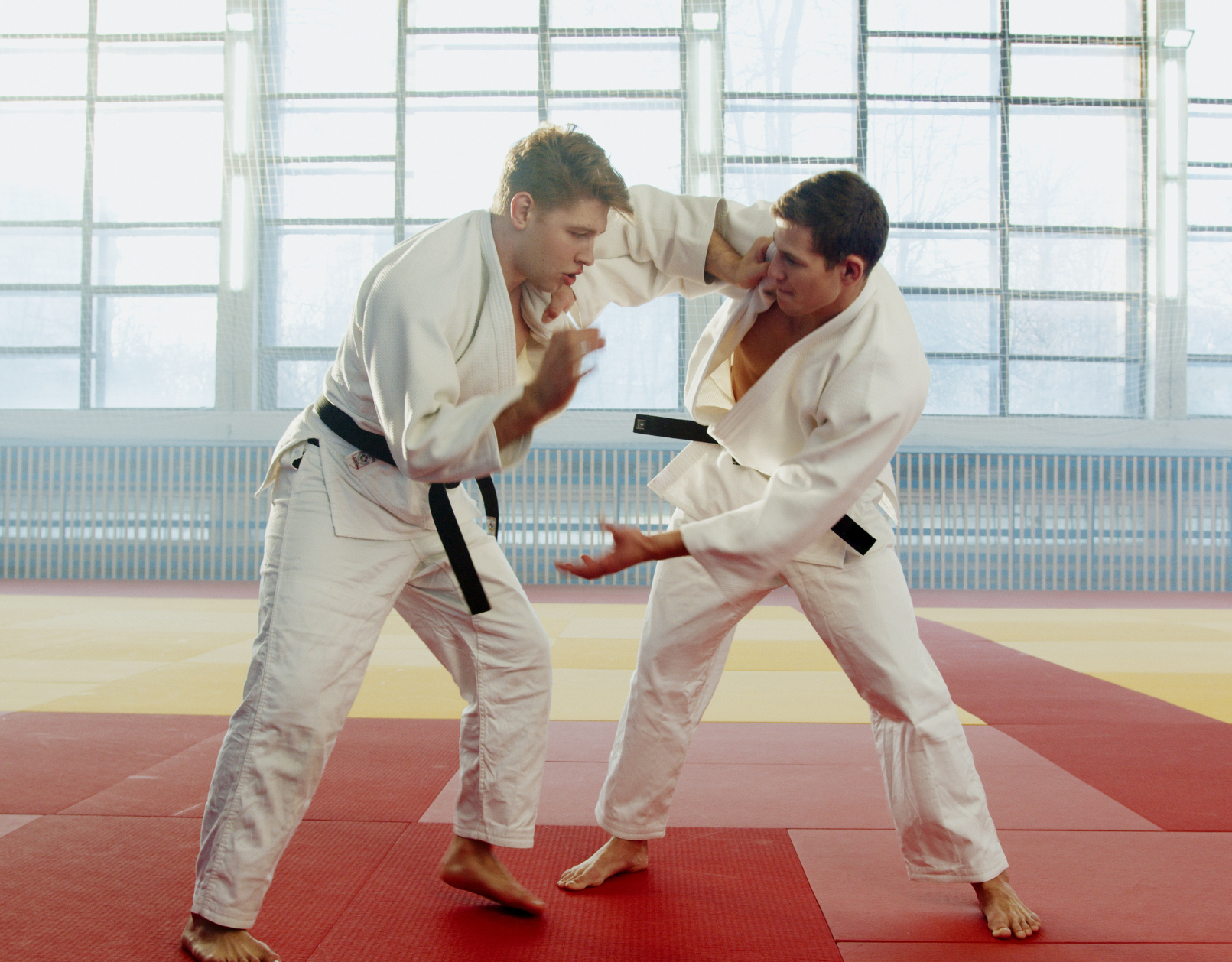 Two men are practicing judo on a mat in a gym.