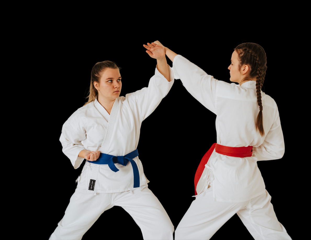 Two women in karate uniforms are fighting each other . one has a blue belt and the other has a red belt.