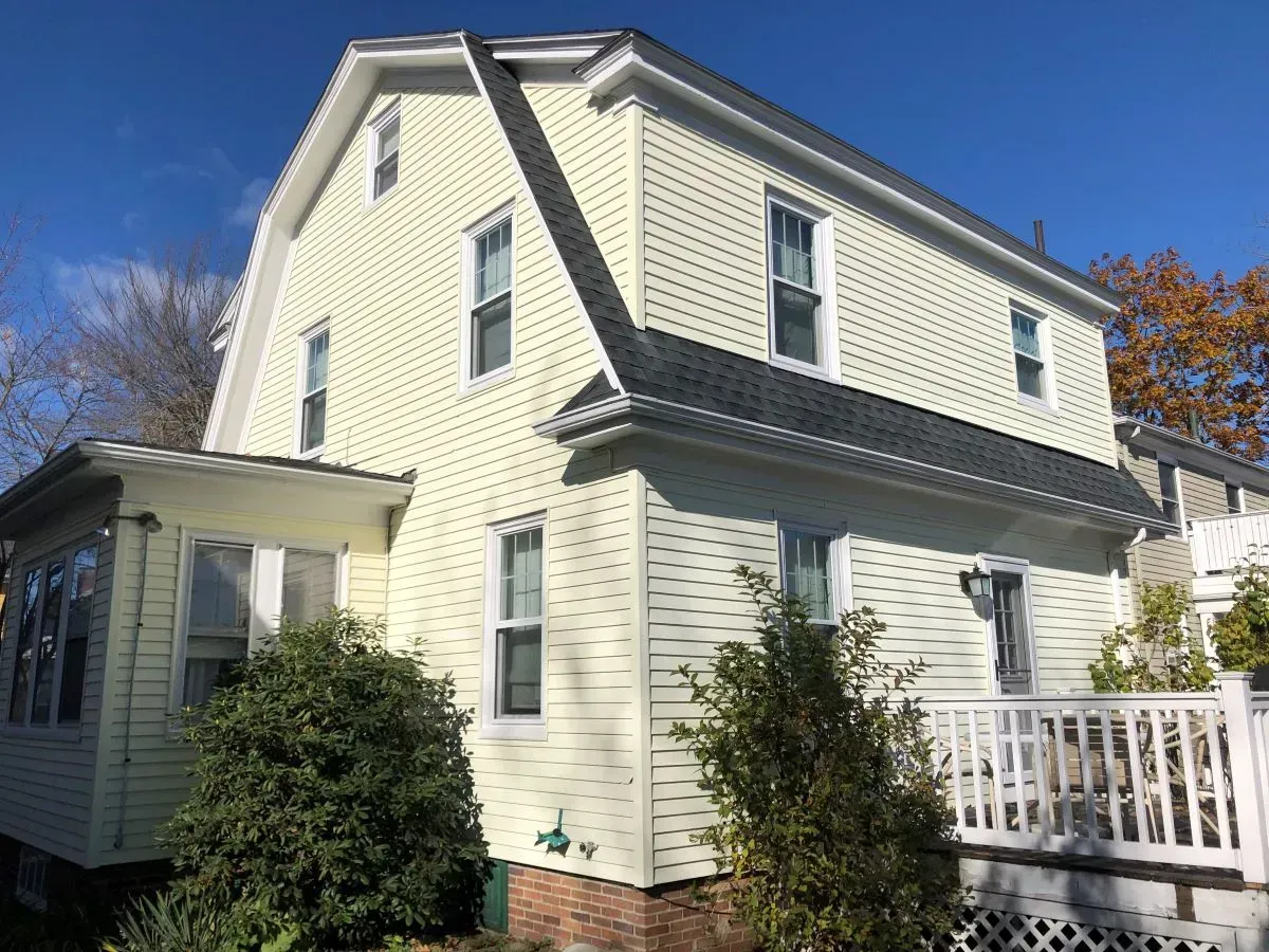 A large yellow house with a white porch and a blue sky in the background.