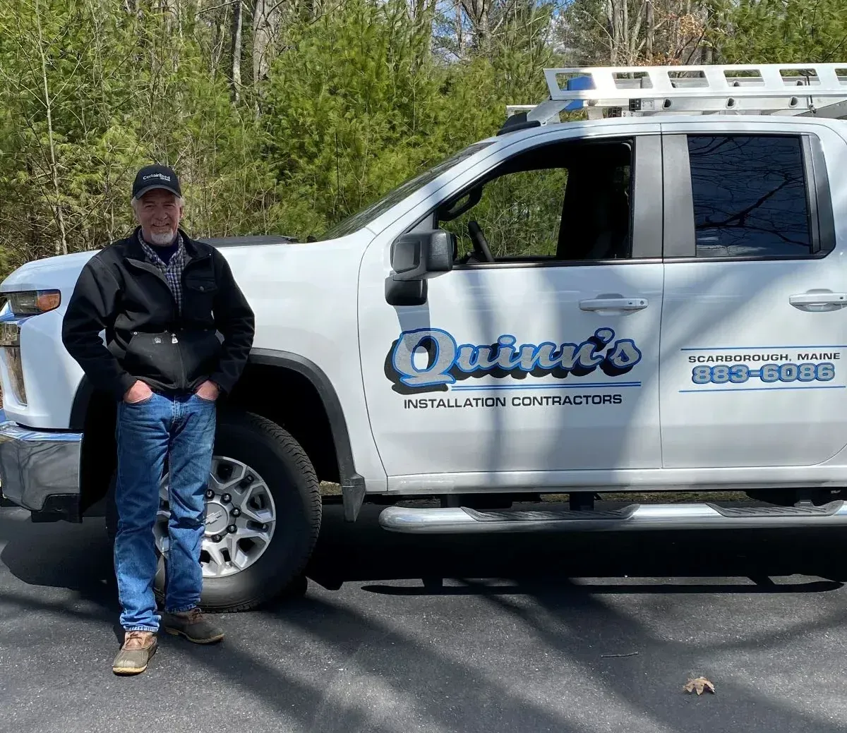 A man is standing in front of a truck that says quince 's